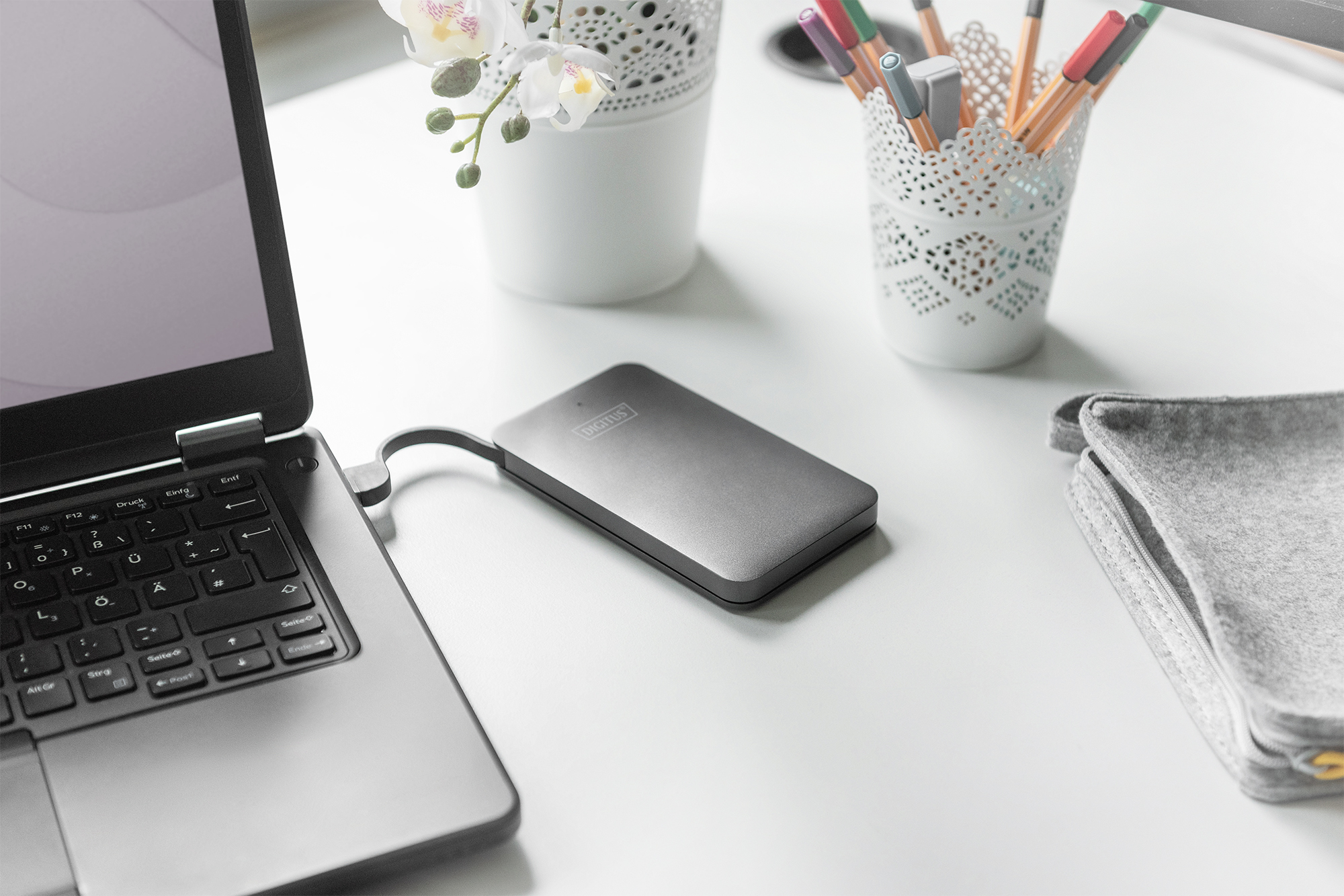 Laptop podłączony do szarego zewnętrznego dysku twardego na białym biurku z akcesoriami.