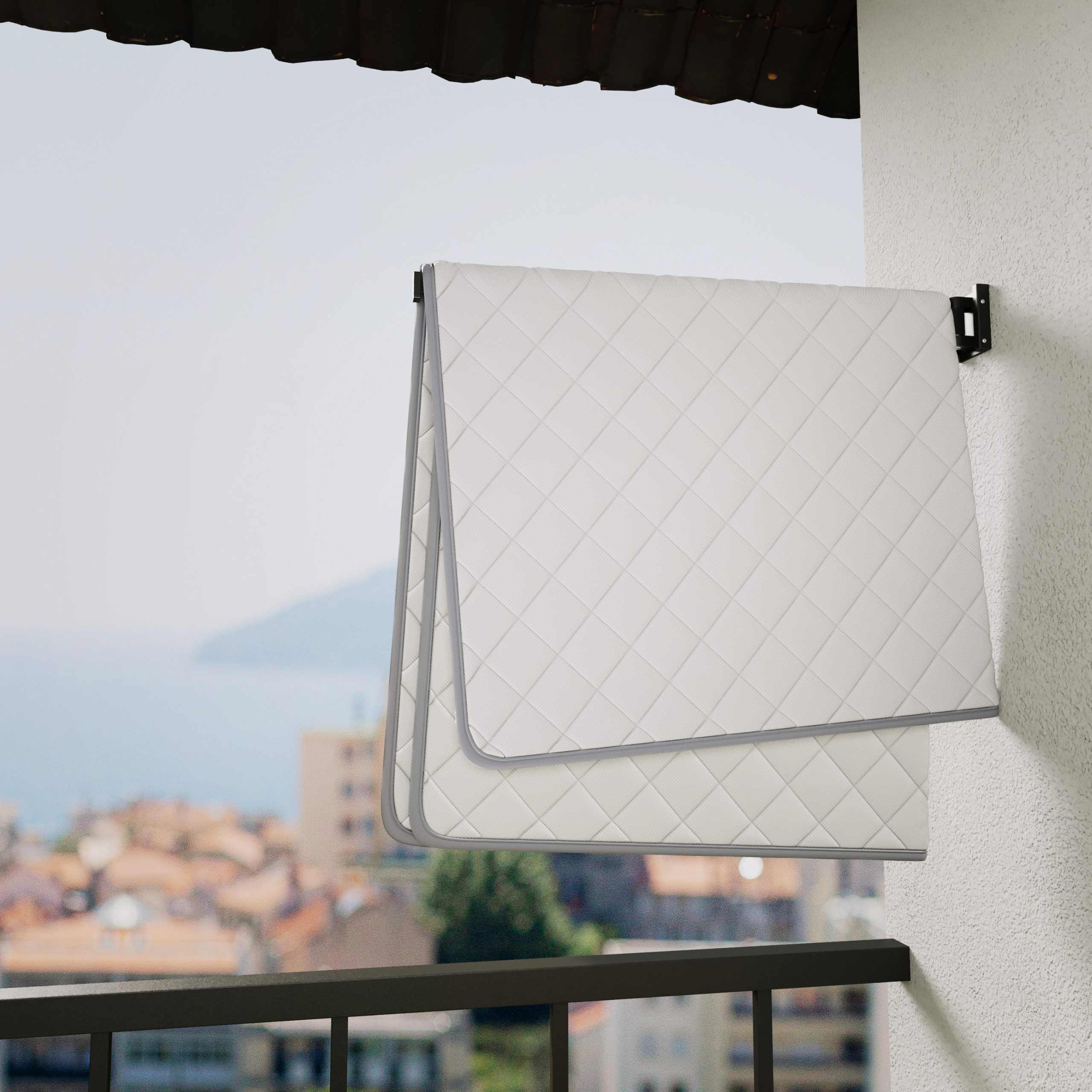 Une couverture blanche avec une bordure grise suspendue sur un balcon, donnant sur une ville et la mer.