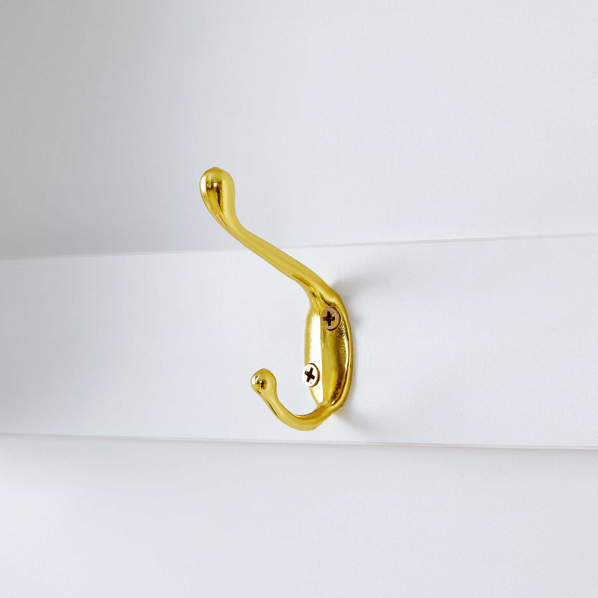 Ein goldfarbener Metallhaken ist an einer weißen Wand befestigt. Es ist ein Kleiderhaken mit geschwungenem Design.