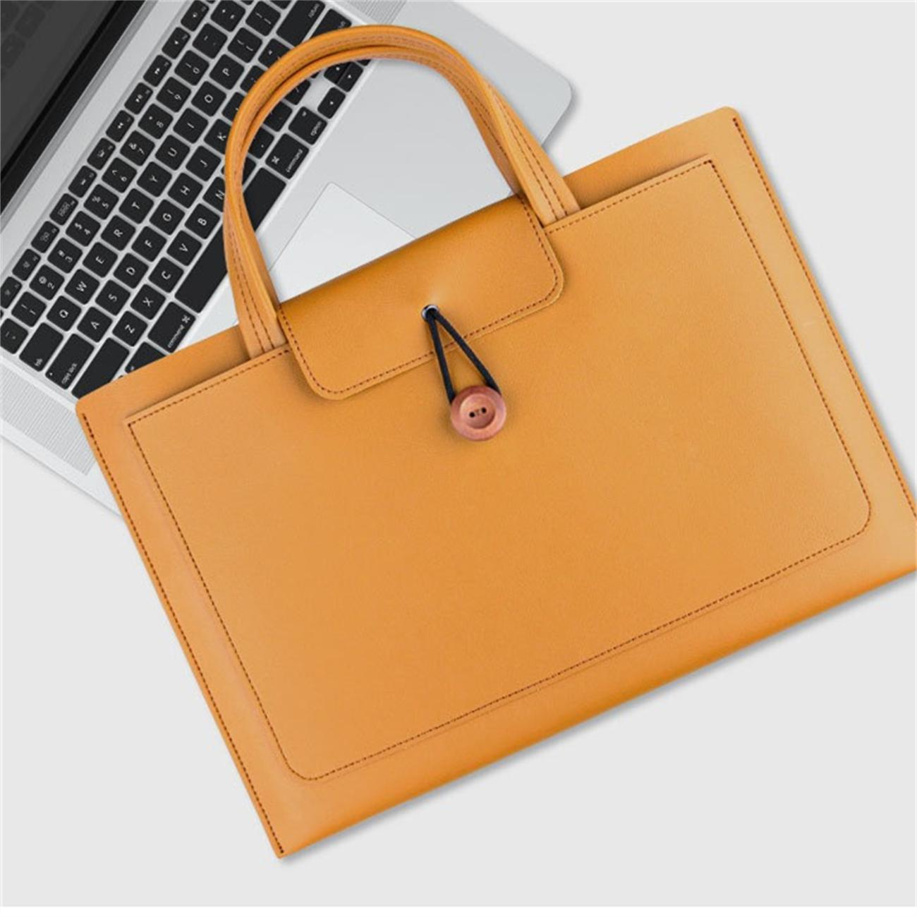 Gelb-orange Ledertasche auf einem Laptop. Die Tasche ist mit einem Knopf verschlossen.