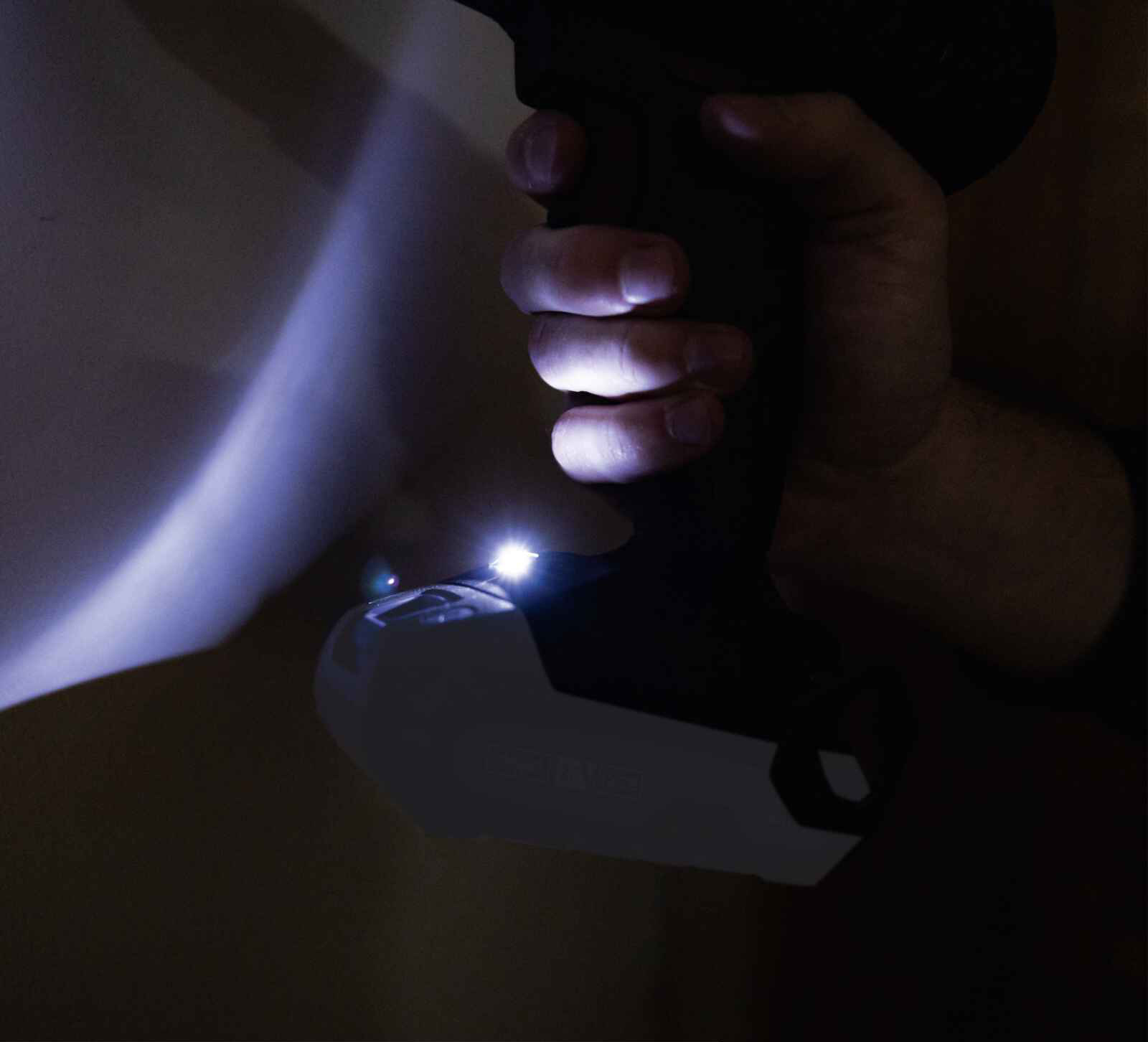 A person's hand holds a black and gray power drill, with two lights shining on a white surface.