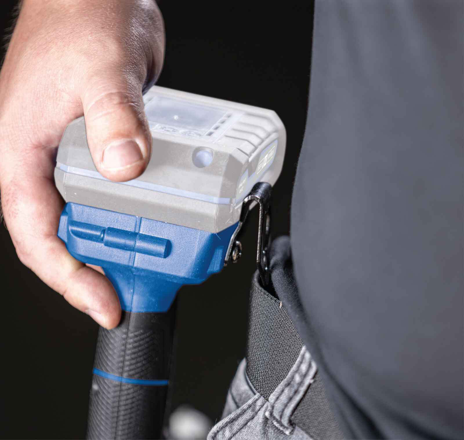 A person's hand holding a device attached to their belt, close-up shot.