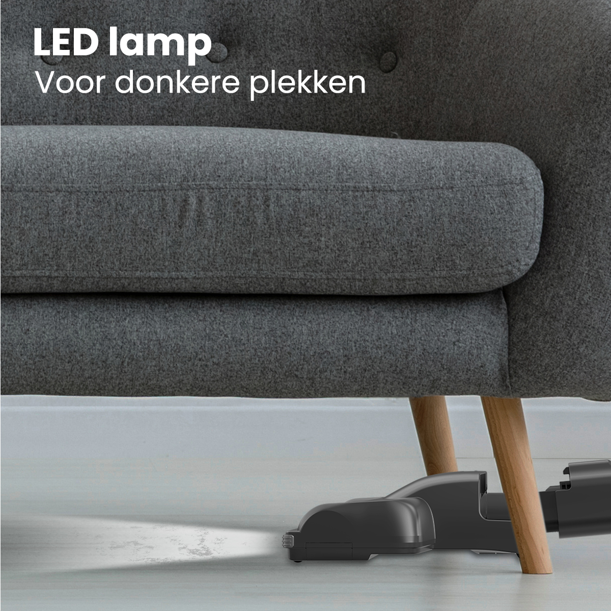 Gros plan d'une tête d'aspirateur sous un canapé gris, montrant la lumière de la lampe LED.