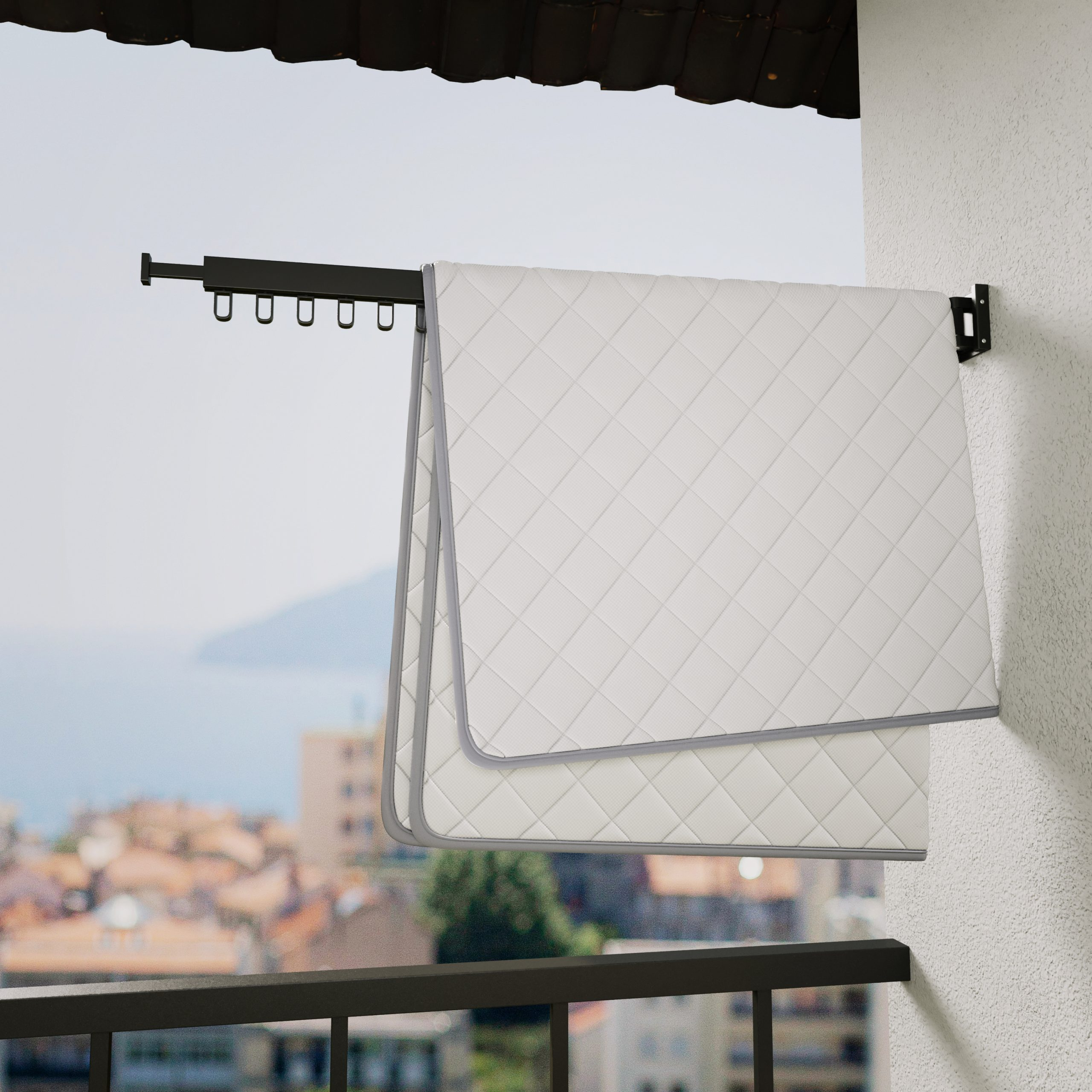 A white quilt drying on a black clothesline on a balcony. A view of the sea in the background.