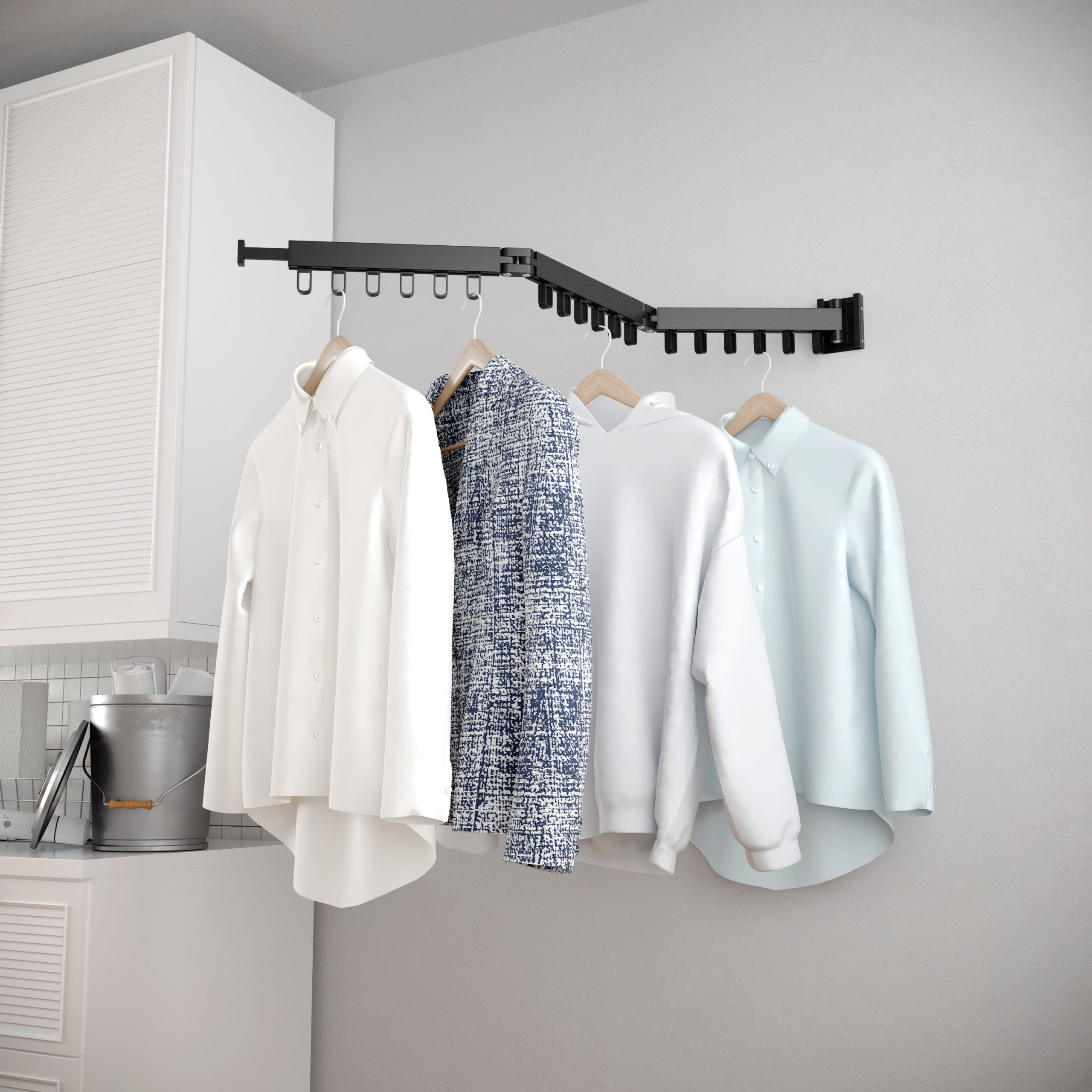 Clothes hanging on a wall-mounted rack in a white room, with a bucket on the floor.