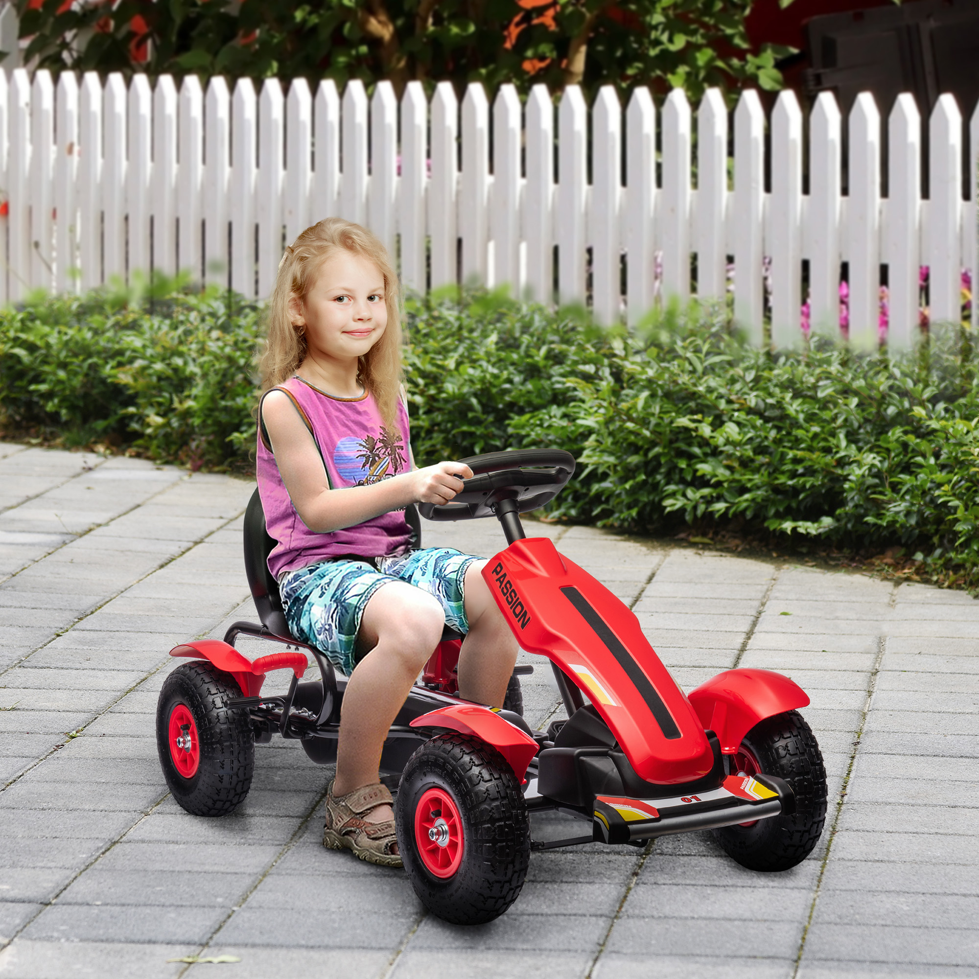 Una bambina guida un go-kart rosso su una superficie pavimentata vicino a una staccionata bianca.