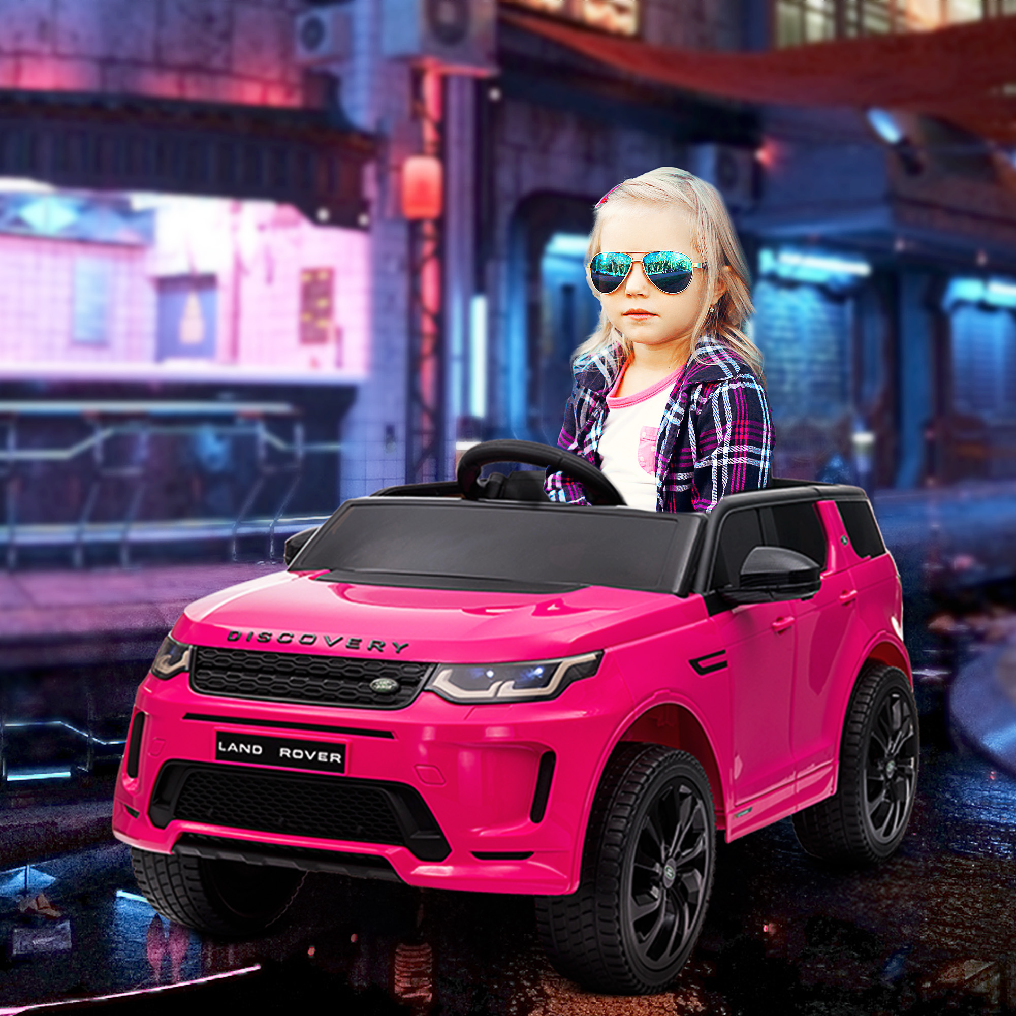 Una niña con gafas de sol conduce un coche de juguete Land Rover rosa en una calle de la ciudad.
