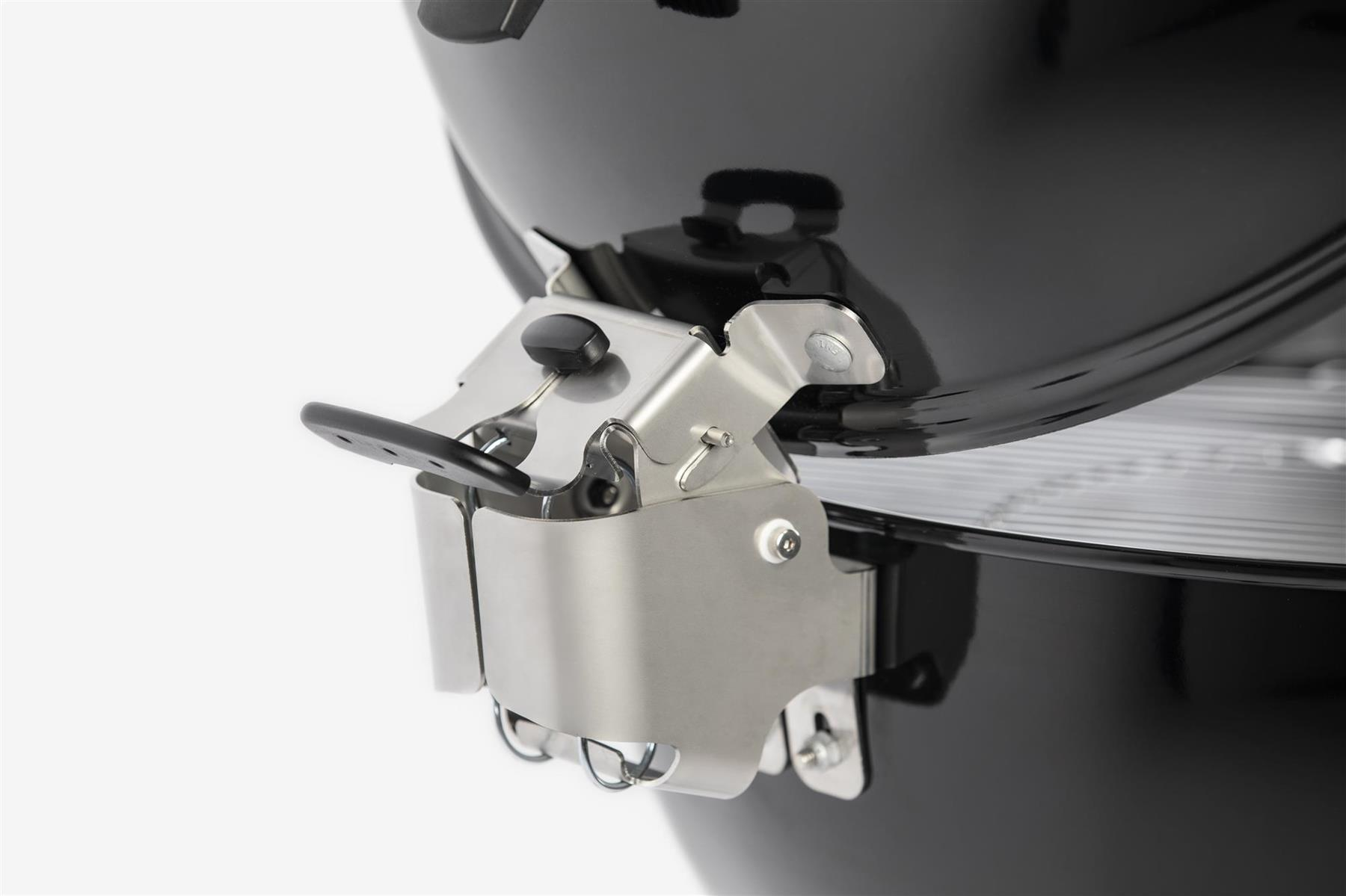 Zbliżenie elementu grilla, pokazujące metalowe części i czarny uchwyt.