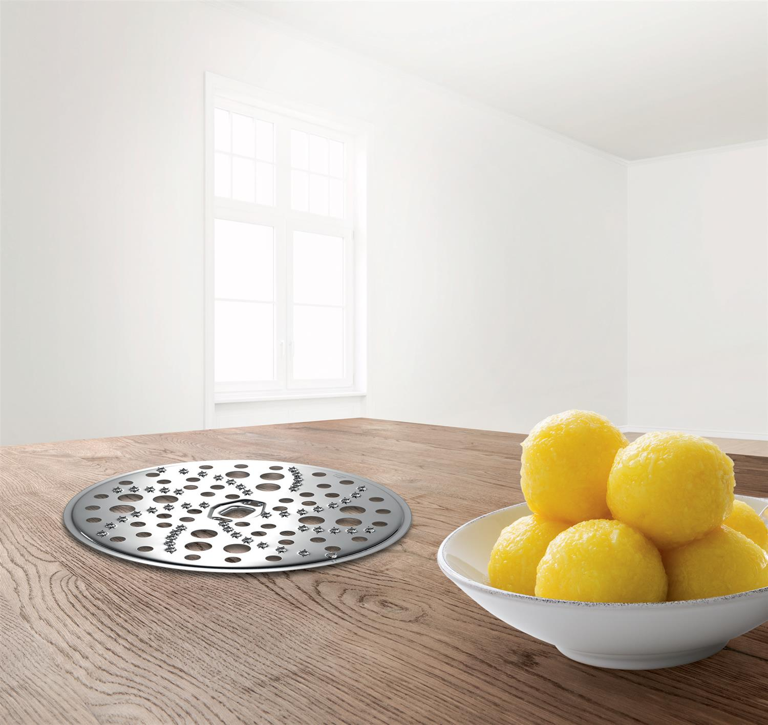 Miska z pierogami i metalowy talerz na drewnianym stole blisko okna.