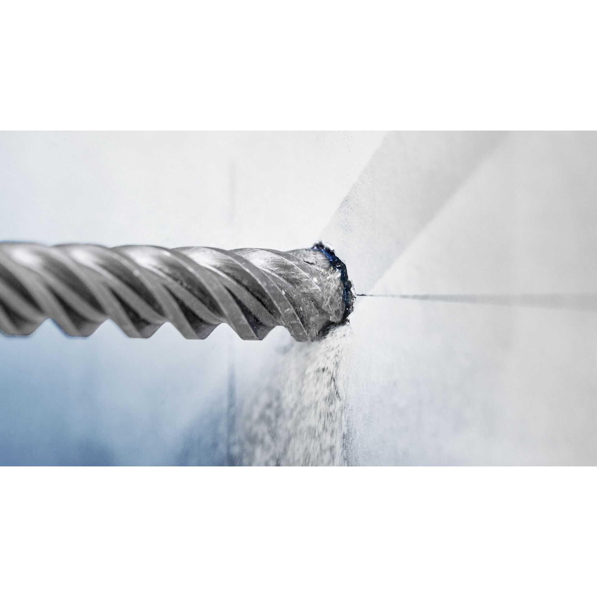 Wiertło wierci otwór w jasnoniebieskiej ścianie. Pył wydobywa się z otworu.