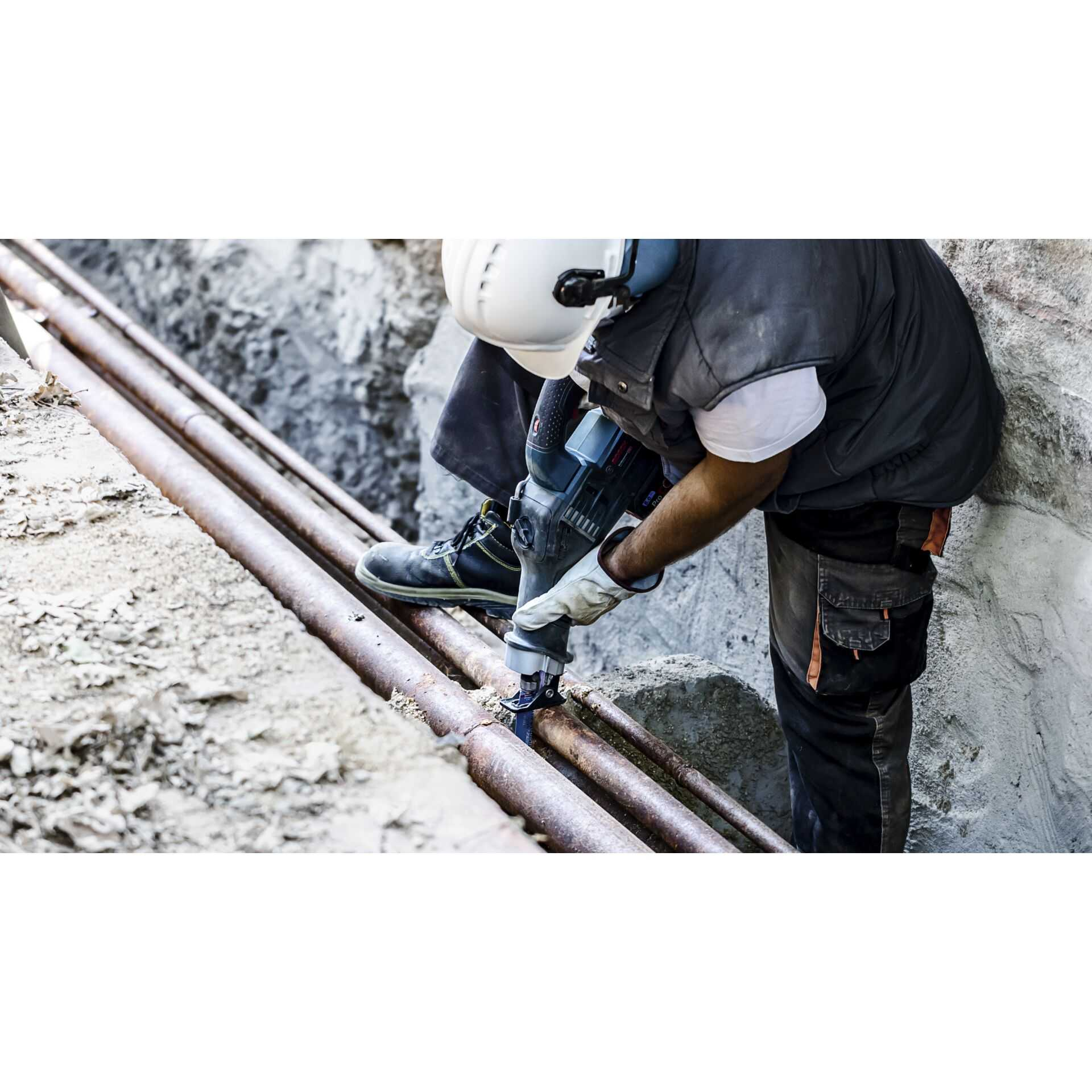 Mężczyzna wierci w metalowych rurach. Widoczne iskry i gruz. Tło jest rozmyte.