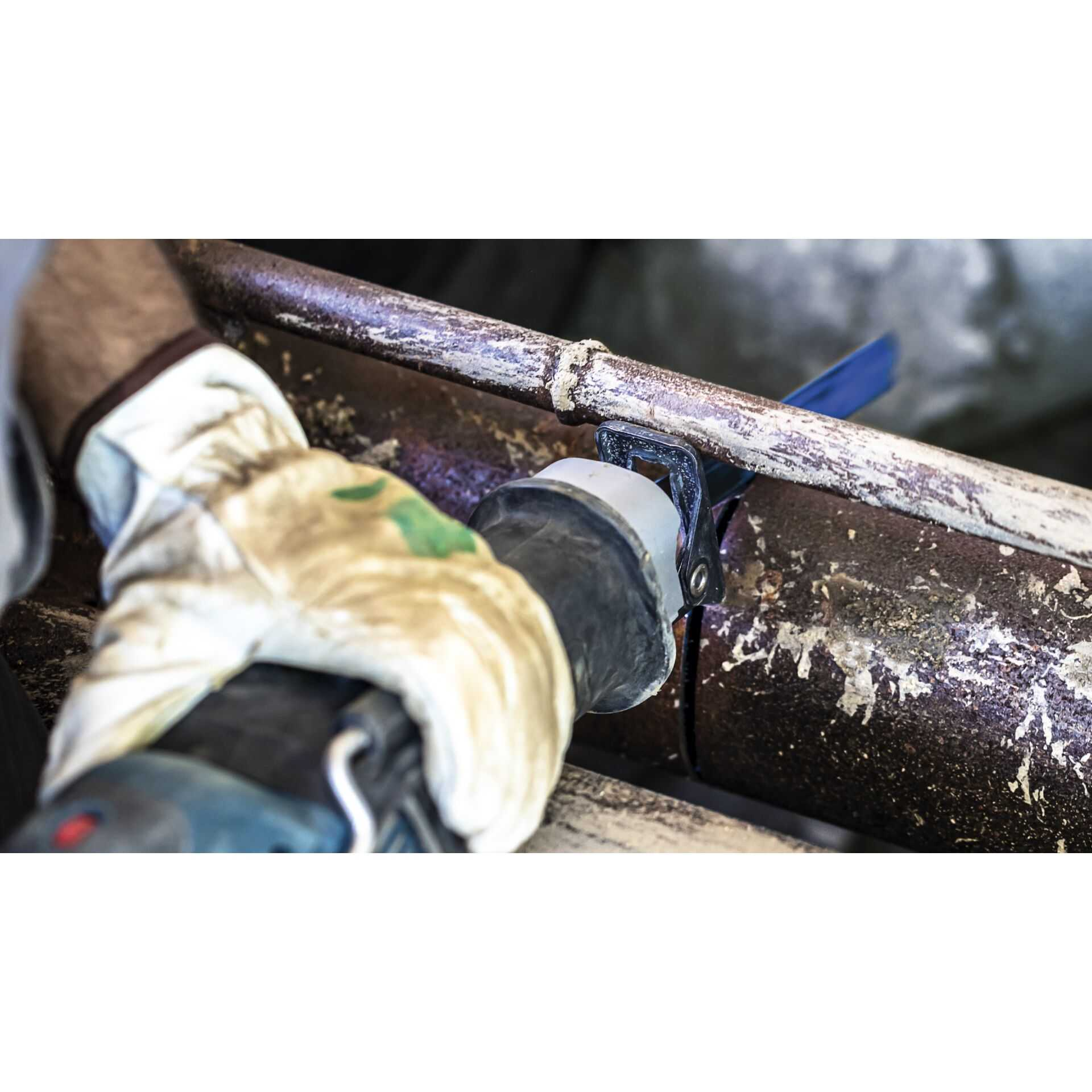 Piła przecina zardzewiałą rurę. Iskry lecą. Tło jest rozmyte.