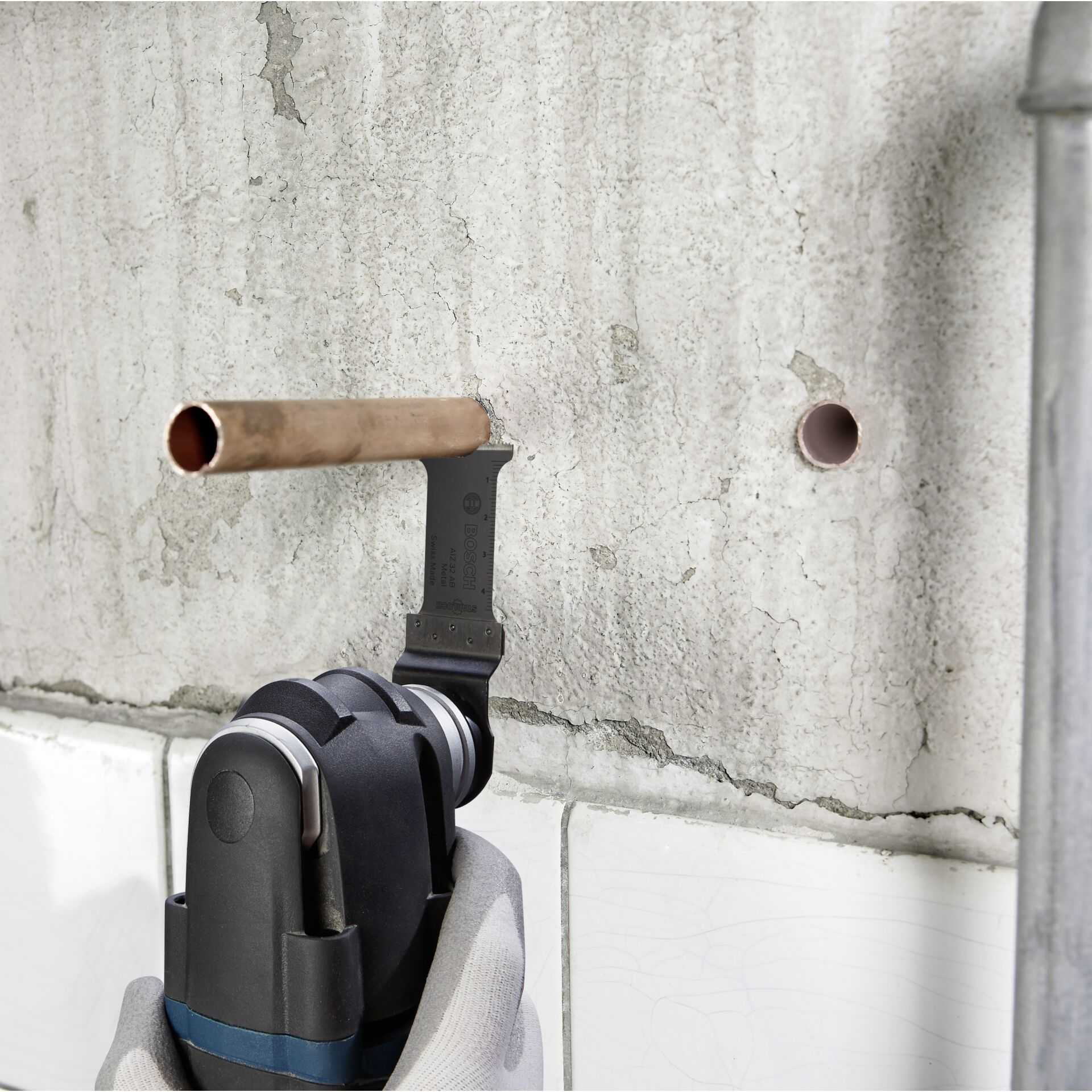 A tool cutting a copper pipe in a concrete wall. The tool is black and silver.