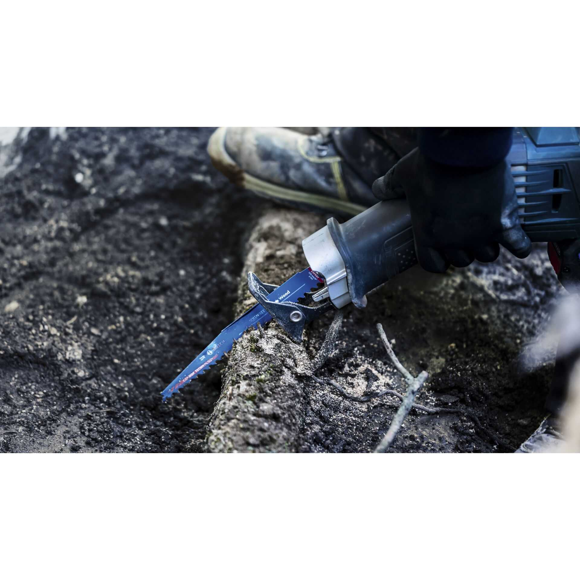 Piła szablasta tnie ciemny pień. Ostrze jest niebieskie. Piła trzymana jest przez osobę.