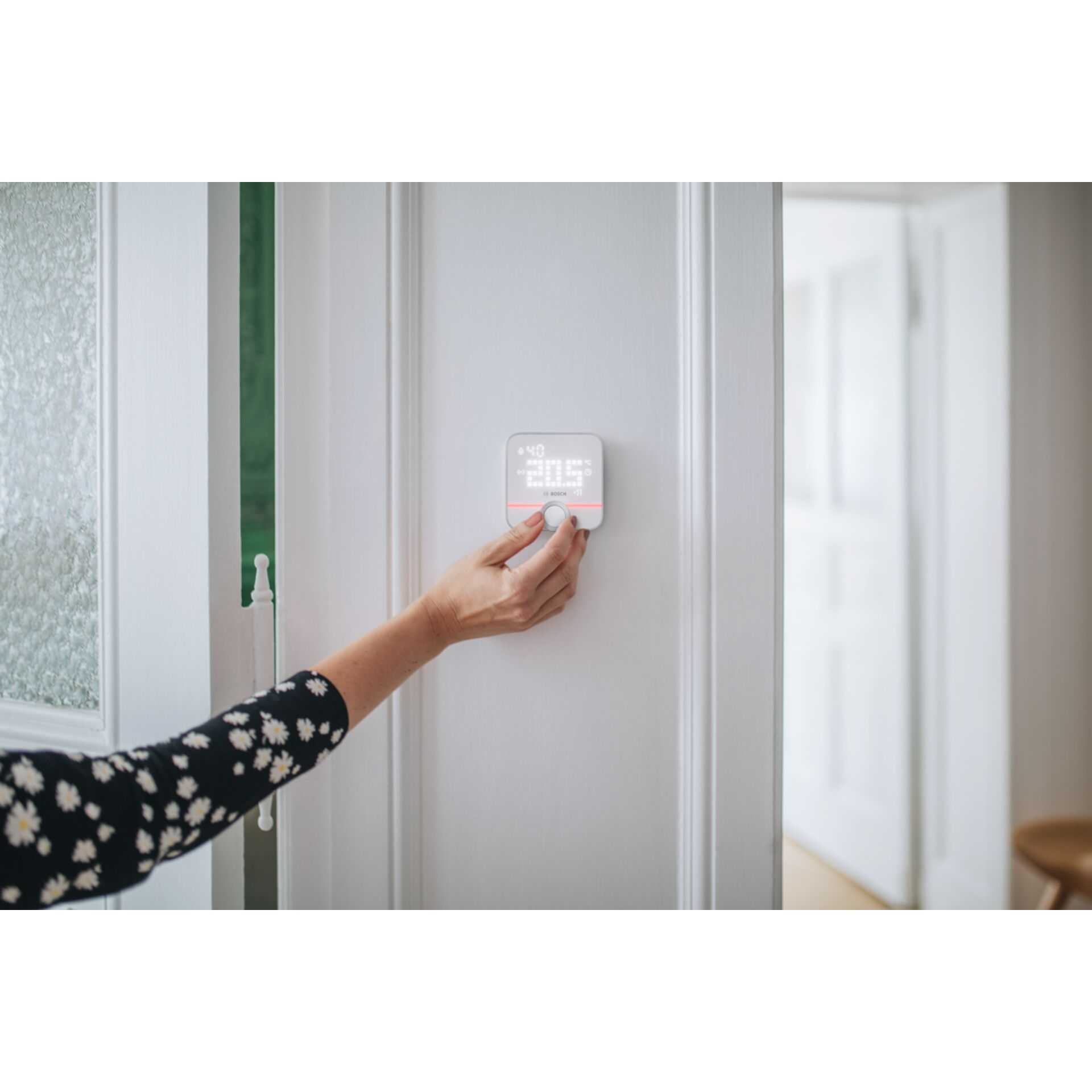 Eine Frau stellt einen intelligenten Thermostat an einer weißen Tür ein. Das Display zeigt eine Temperatur.