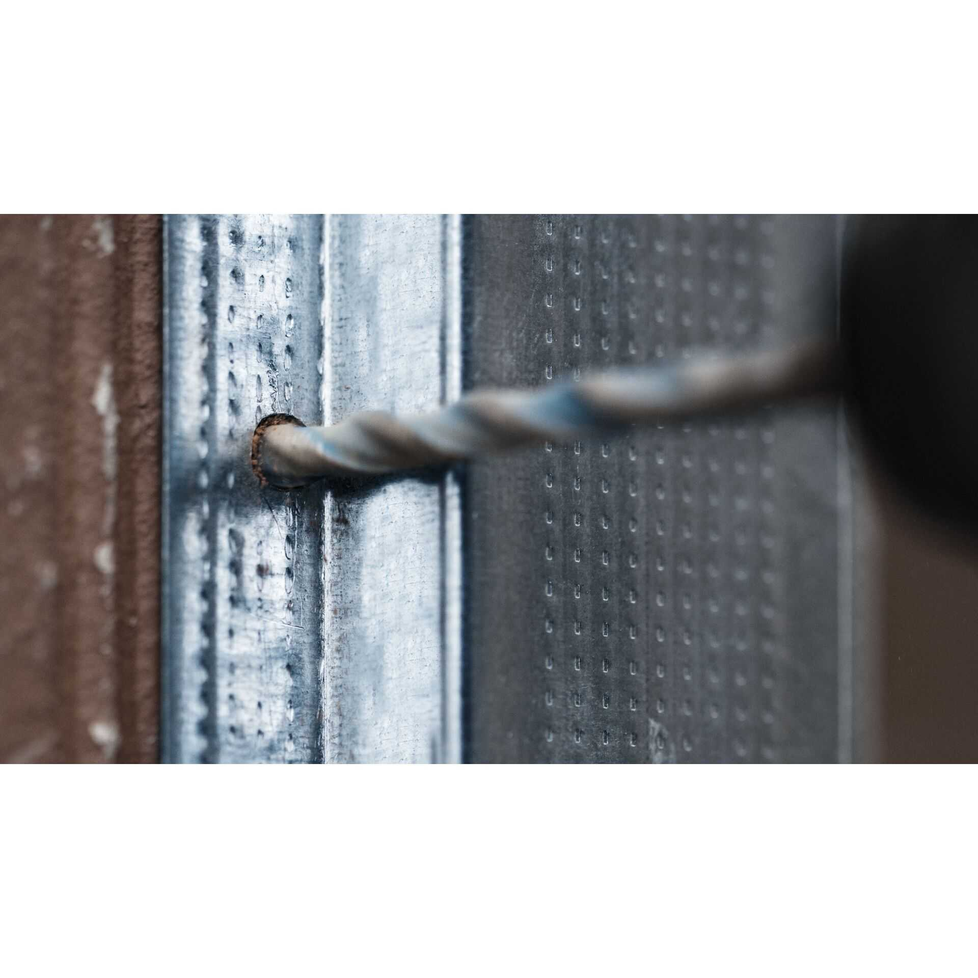 Wiertło wierci w metalowej ścianie szkieletowej.