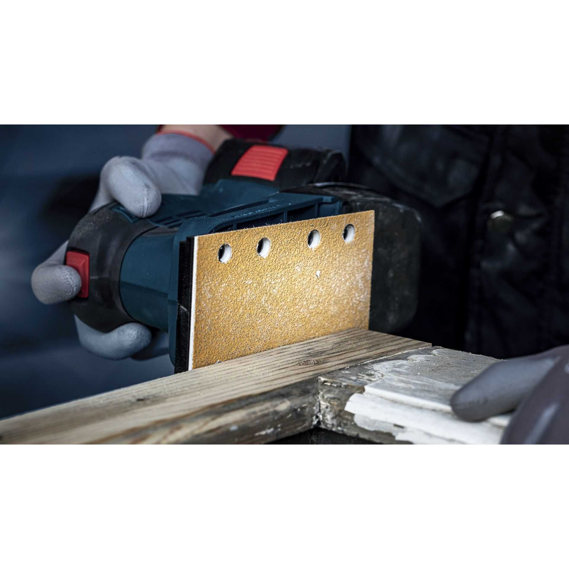 Una persona leviga una tavola di legno con una levigatrice, indossando guanti.