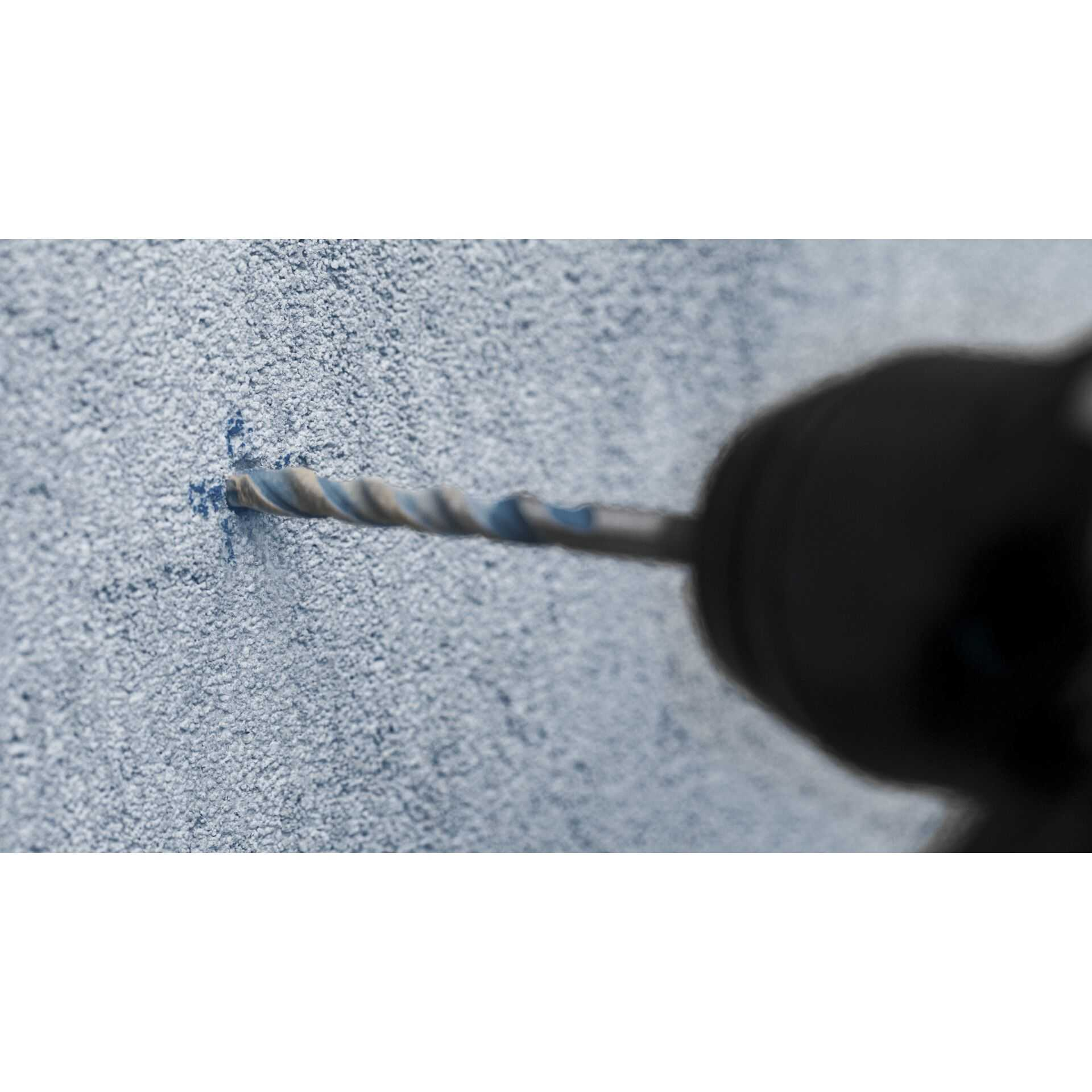 Wiertło wierci w jasnoniebieskiej ścianie. Wiertło jest w prawym rogu.