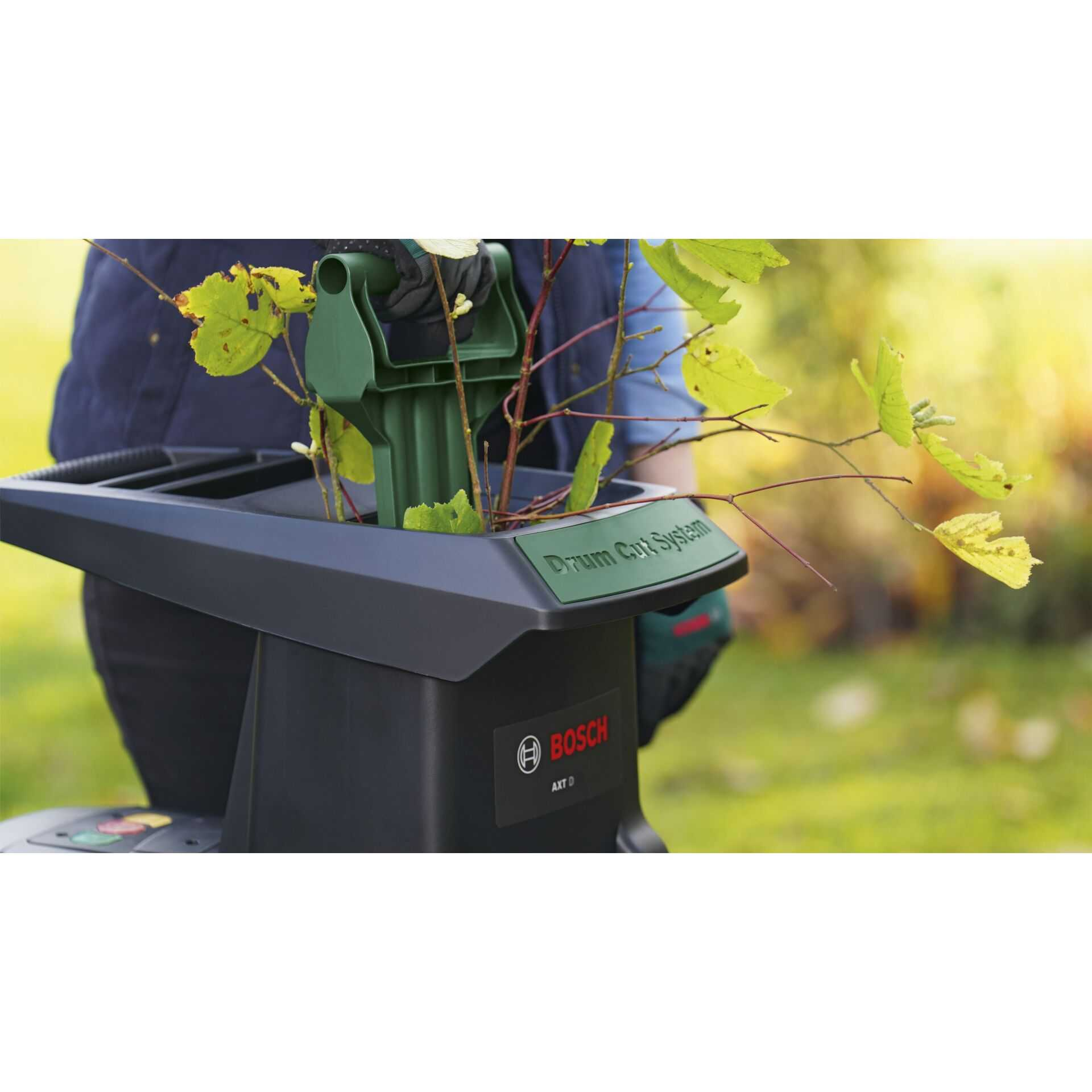 Une personne introduit des feuilles et des branches vertes dans une déchiqueteuse de bois noire et verte.