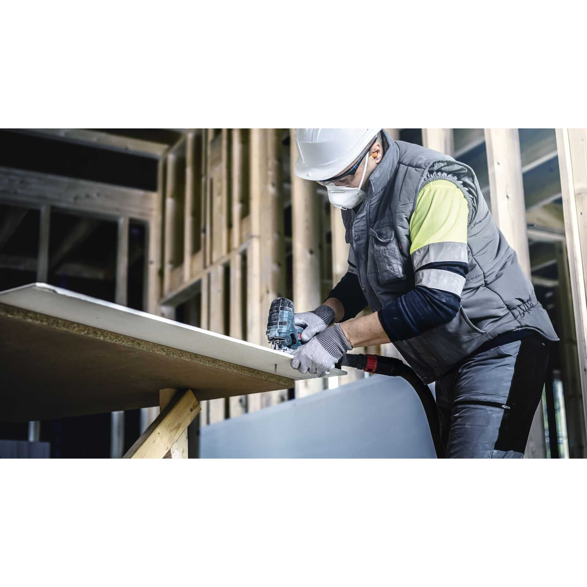 Osoba tnie płytę gipsowo-kartonową piłą. Noszą maskę i okulary ochronne.