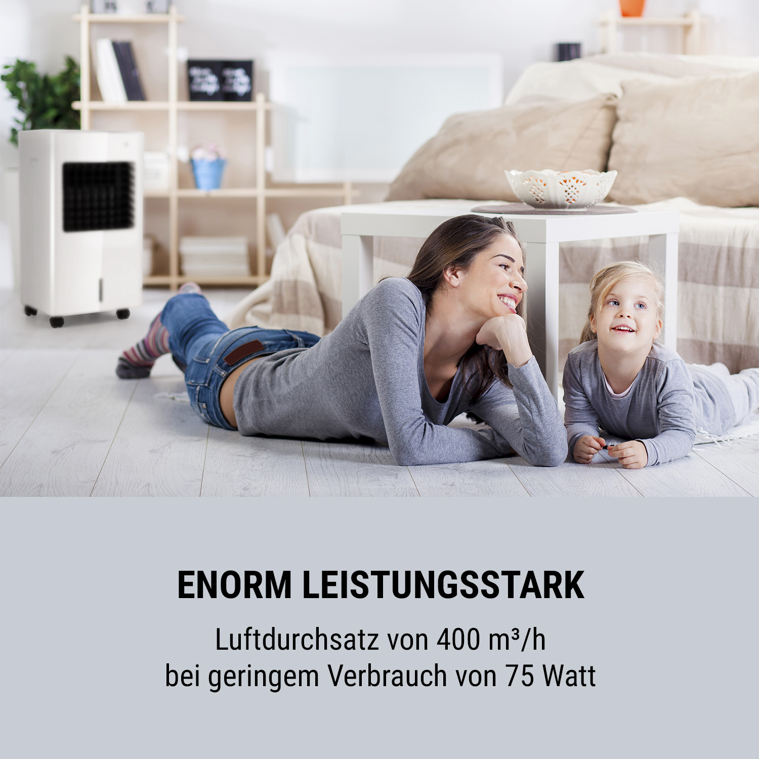 Eine Frau und ein Mädchen liegen auf dem Boden neben einem weißen Luftkühler. Text: ENORM LEISTUNGSSTARK.