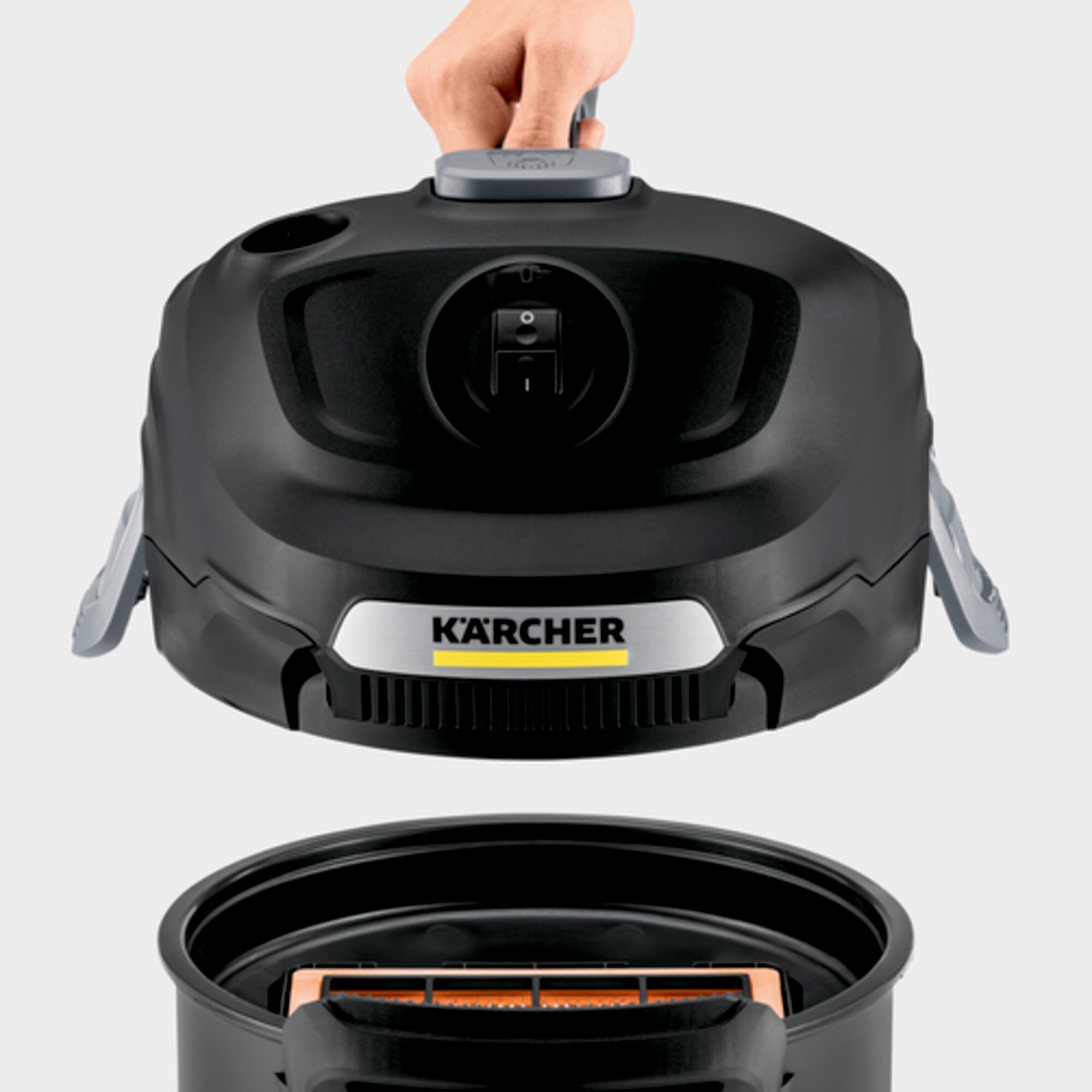 Ręka podnosi górę czarnego odkurzacza. Widoczne logo Kärcher, filtr poniżej.