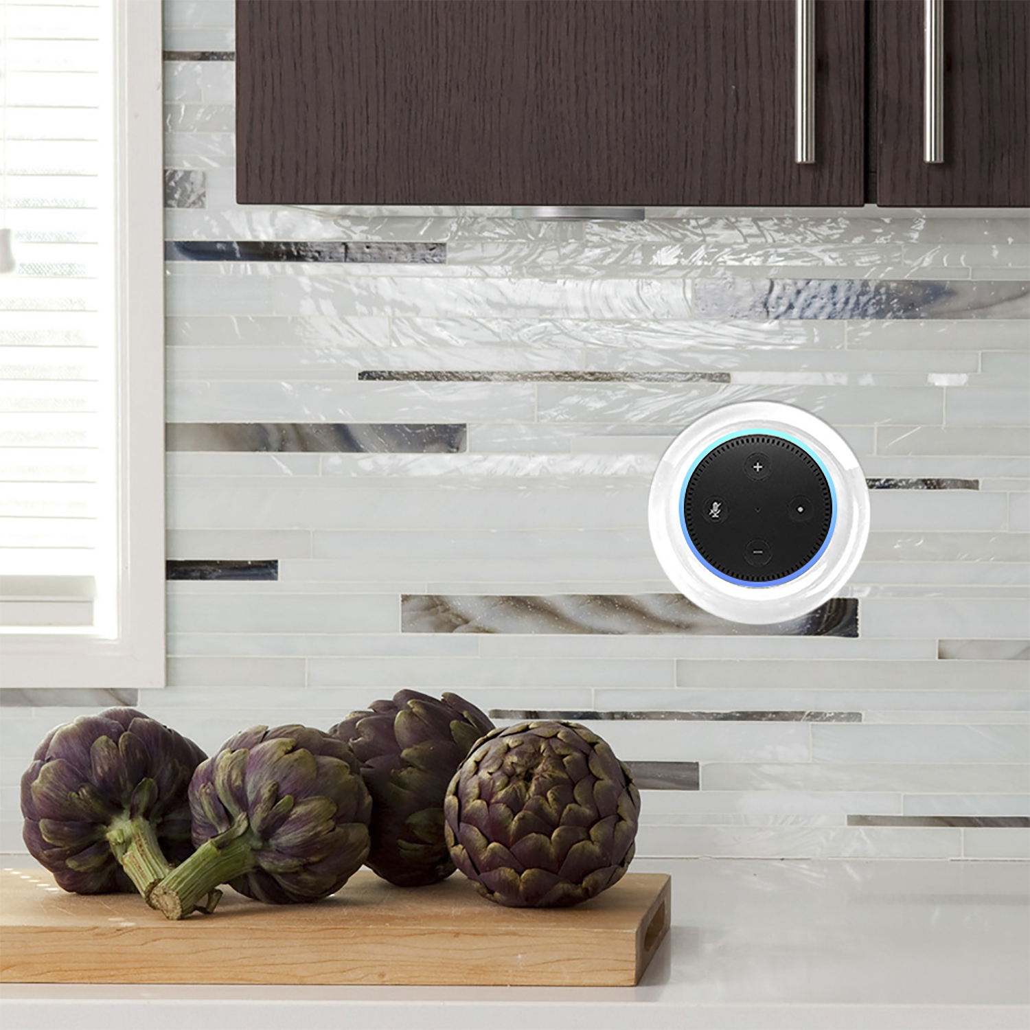Un Echo Dot su una parete della cucina, vicino a carciofi su un tagliere di legno, con paraschizzi di piastrelle bianche.