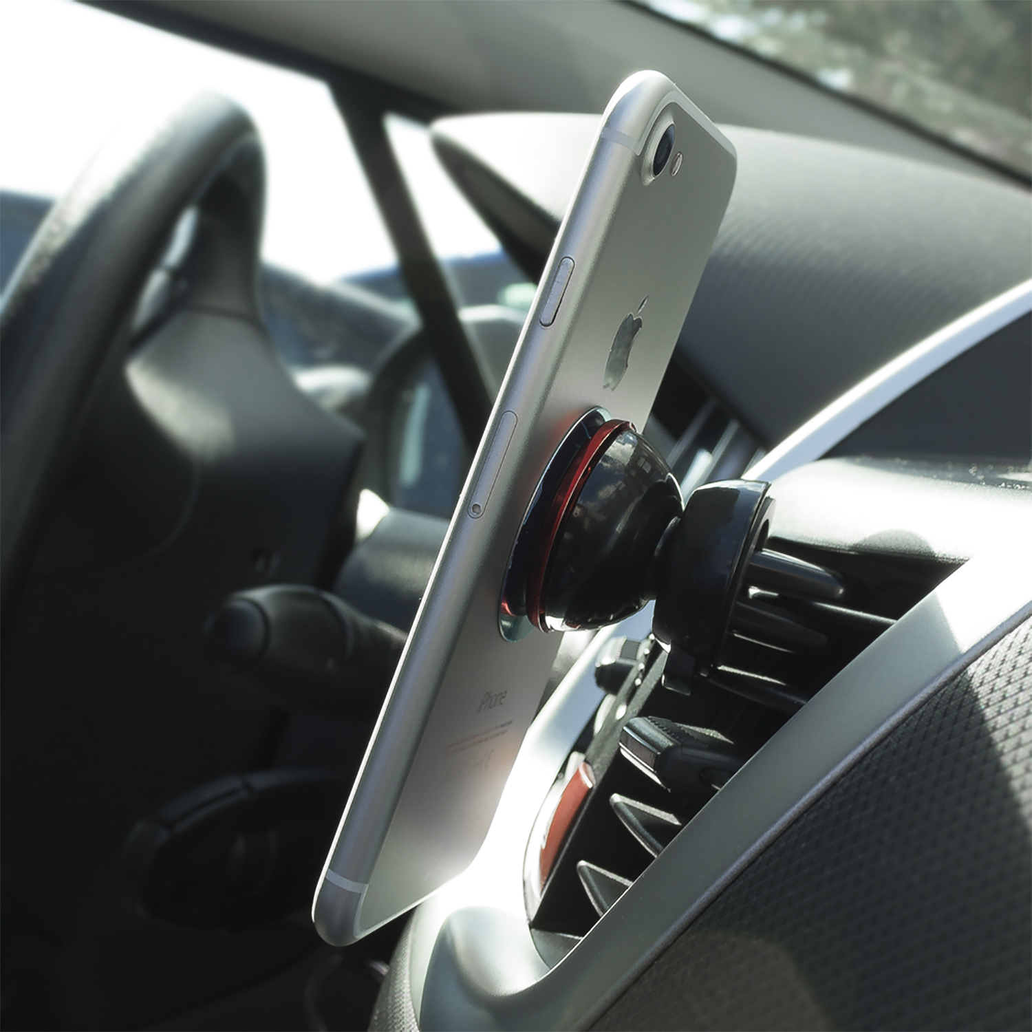 iPhone argento su supporto auto. Supporto nero su bocchetta. Volante sullo sfondo.