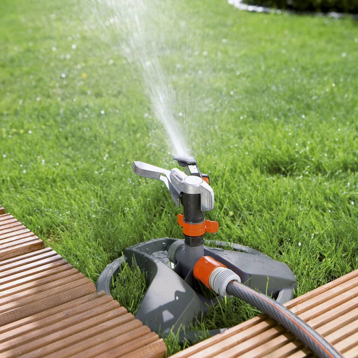Ein Rasensprenger in einem Garten sprüht Wasser auf grünes Gras. Der Rasensprenger steht auf einem grauen Sockel.