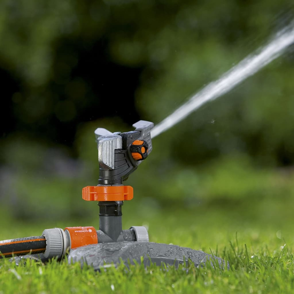 Ein Rasensprenger sprüht Wasser auf grünes Gras. Der Rasensprenger steht auf einem grauen Sockel im Garten.