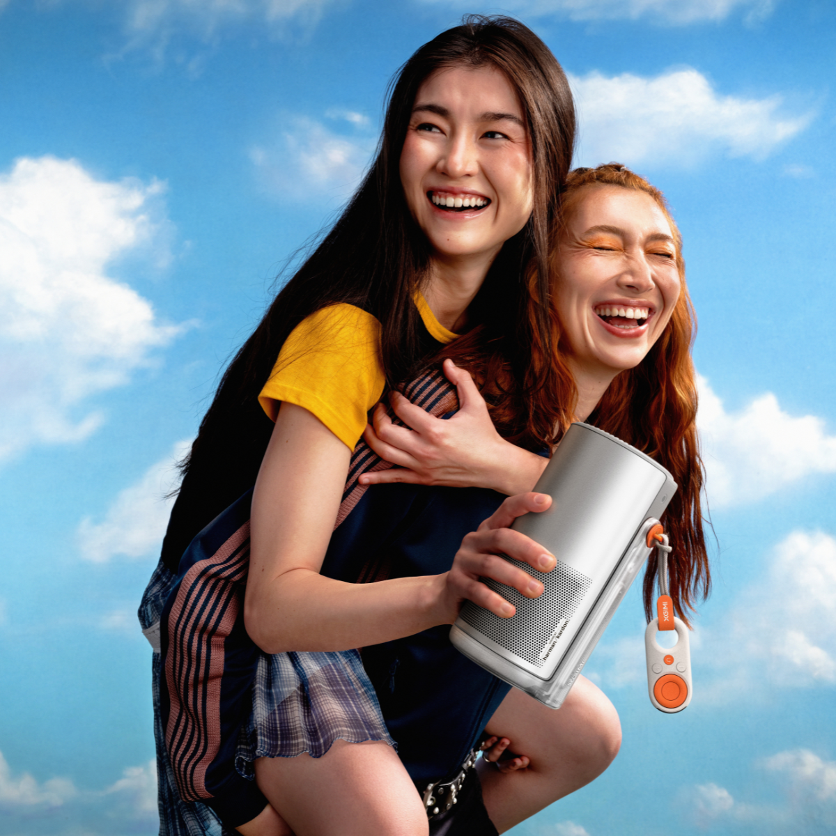 Dwie kobiety śmieją się, jedna niesie drugą. Trzymają głośnik.