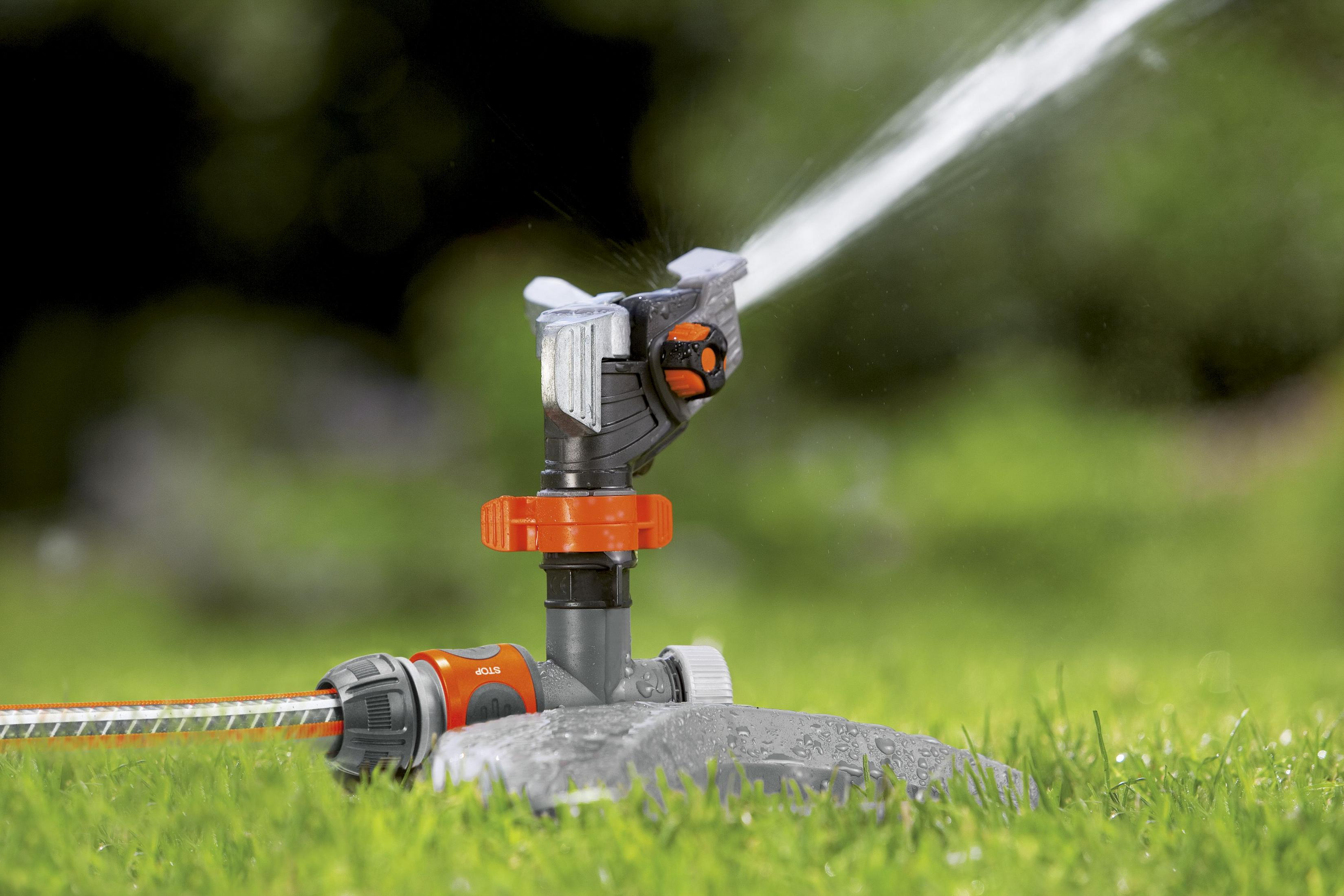 Ein Rasensprenger, der Wasser über grünes Gras in einem Garten sprüht.