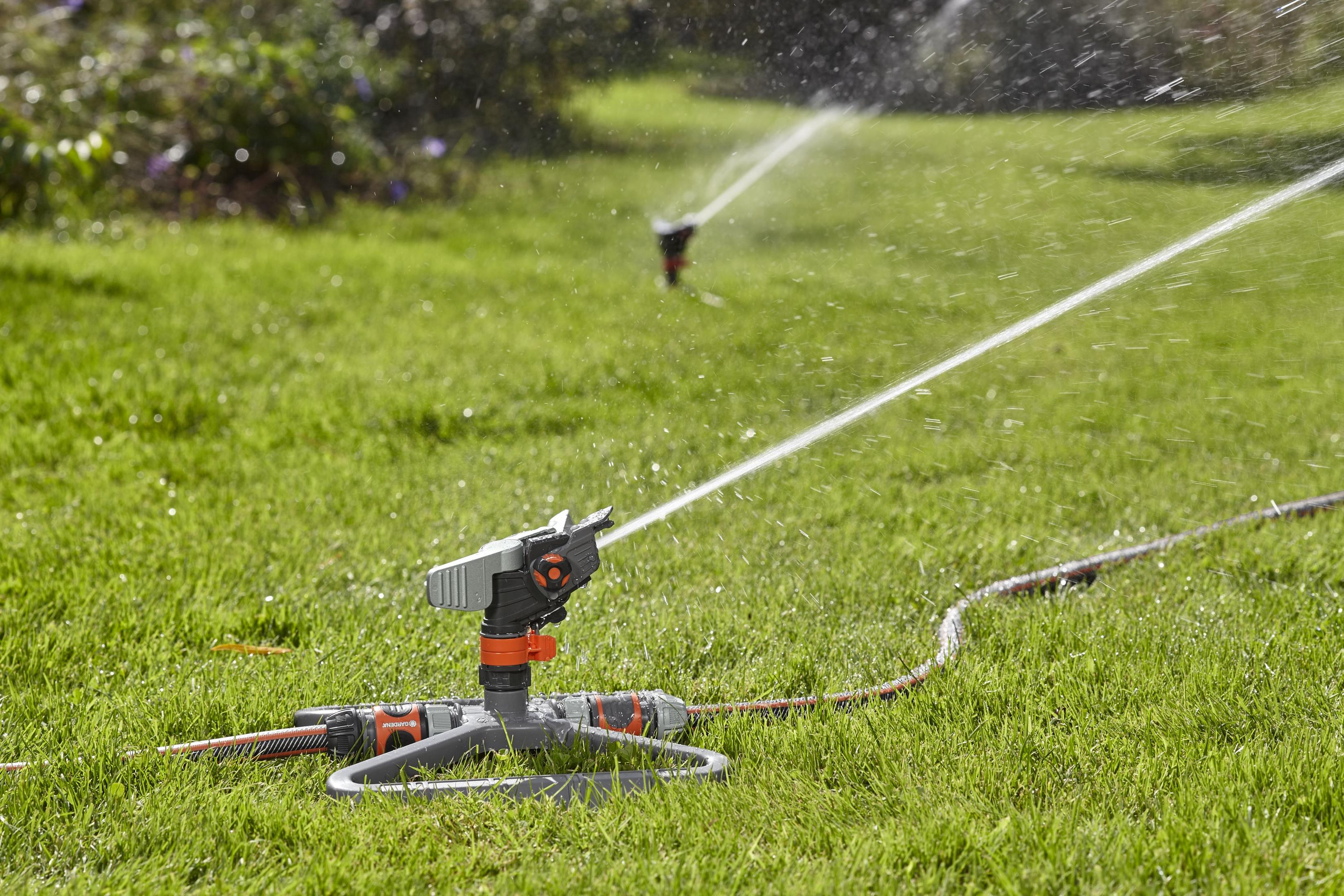 Zwei Rasensprenger bewässern grünes Gras, Wasserstrahlen sind sichtbar.