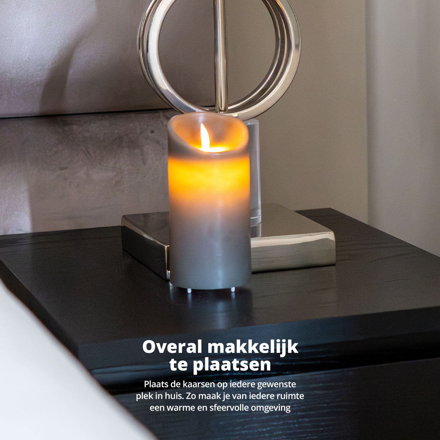 Une bougie grise avec une flamme brillante sur une table de chevet noire avec une lampe argentée.
