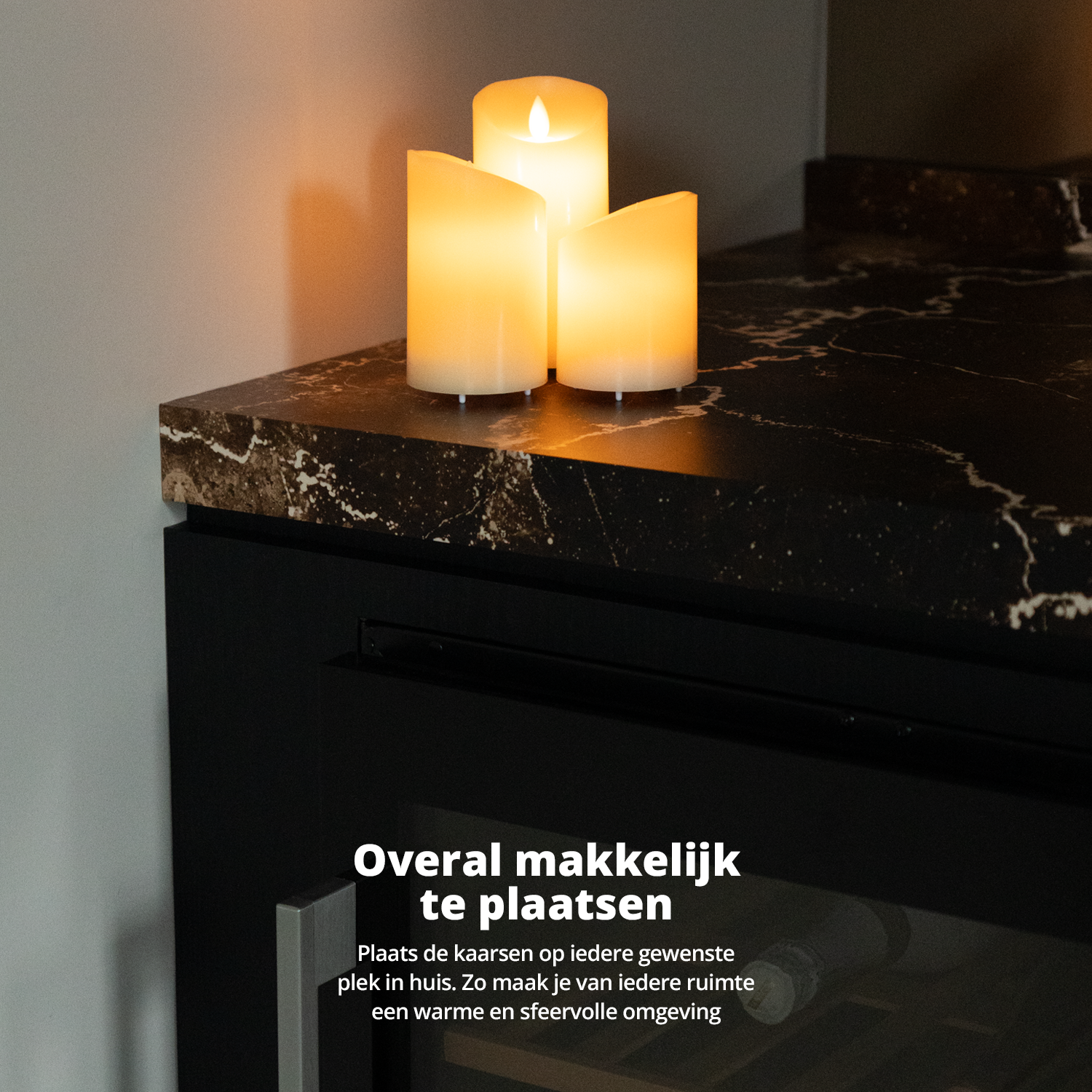 Drie brandende kaarsen op een zwart aanrecht. De achtergrond is een witte muur.