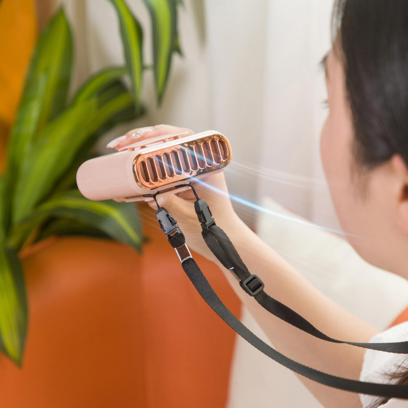 Person hält einen pinkfarbenen Nackenfächer. Es hat einen schwarzen Riemen. Der Ventilator bläst Luft.