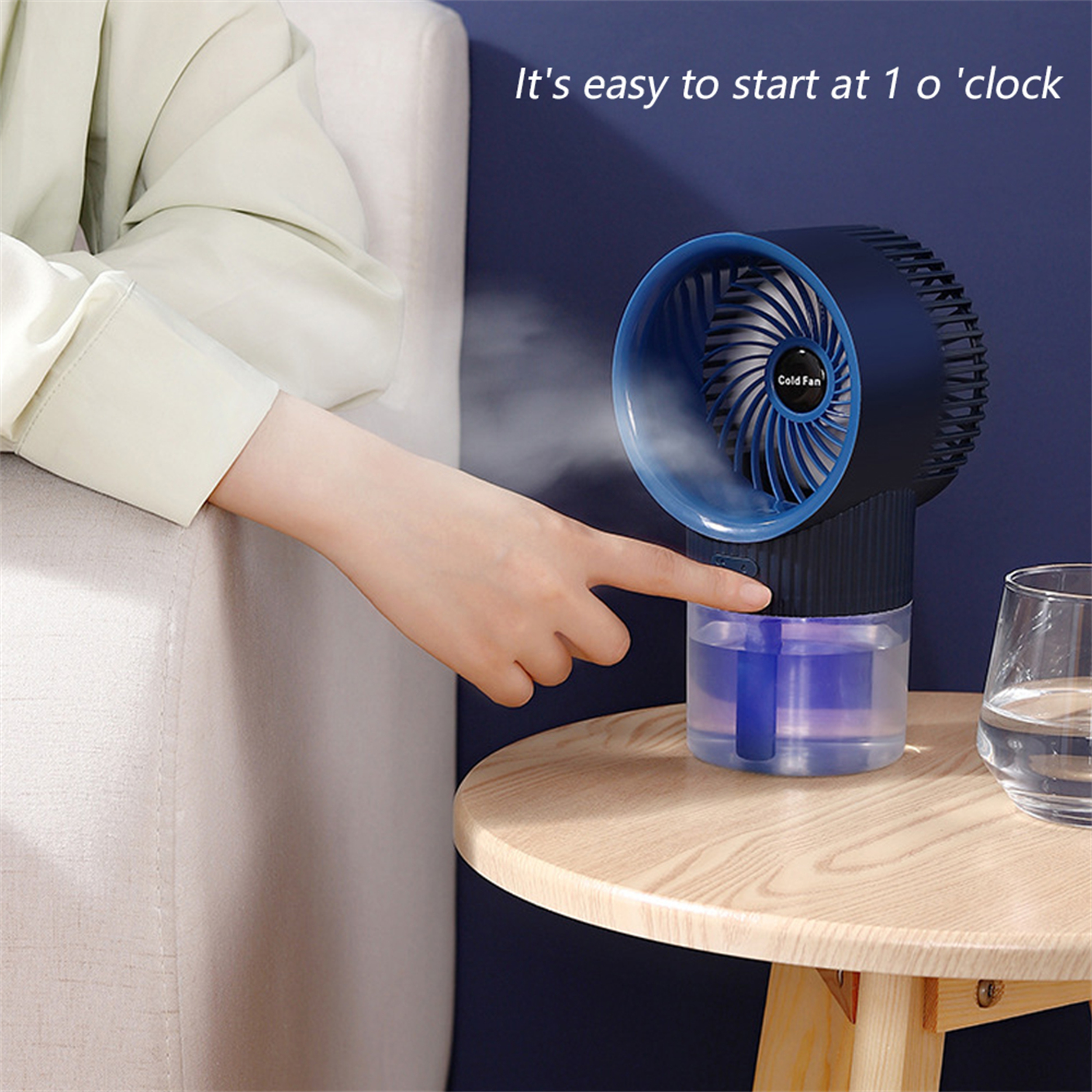 Die Hand einer Person drückt den Knopf eines kalten Ventilators. Ein Glas Wasser steht auf einem Holztisch.
