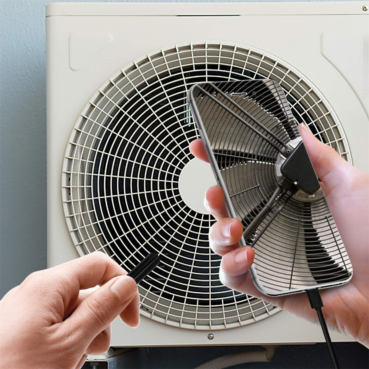 Hand hält ein Telefon mit einem Lüfter, vor einer Wand-Klimaanlage.