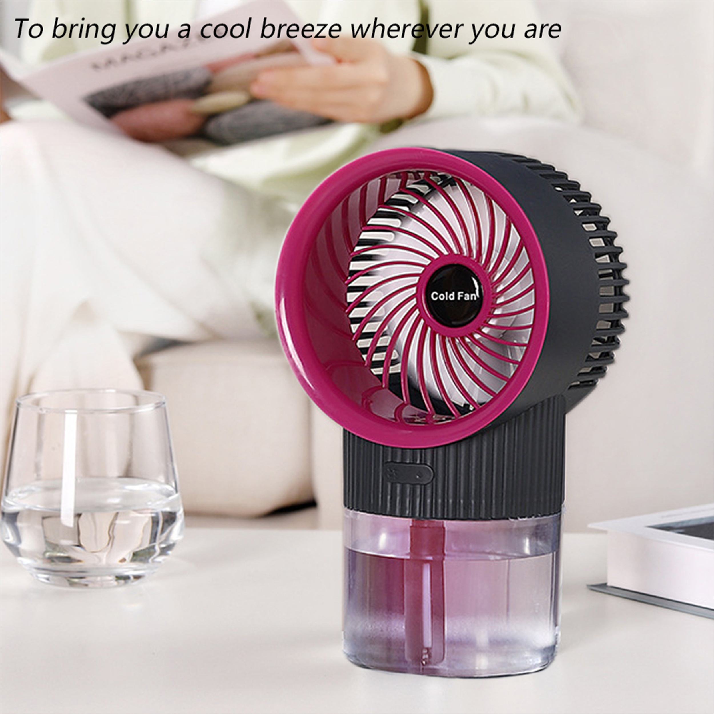 Kleiner Ventilator auf einem Tisch, in der Nähe eines Wasserglases, Person hält Magazin.