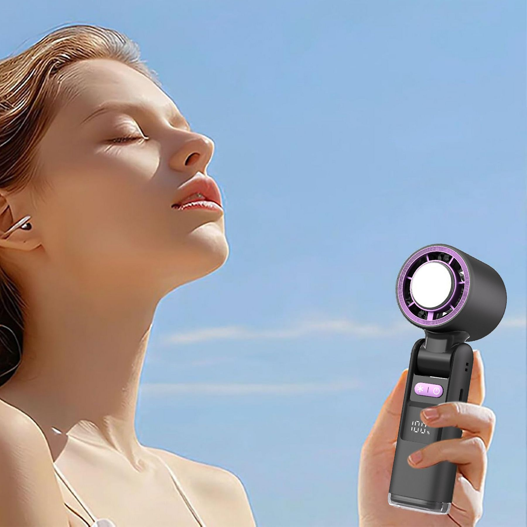 Eine Frau hält einen schwarzen Ventilator vor ihr Gesicht, im Hintergrund ein blauer Himmel.