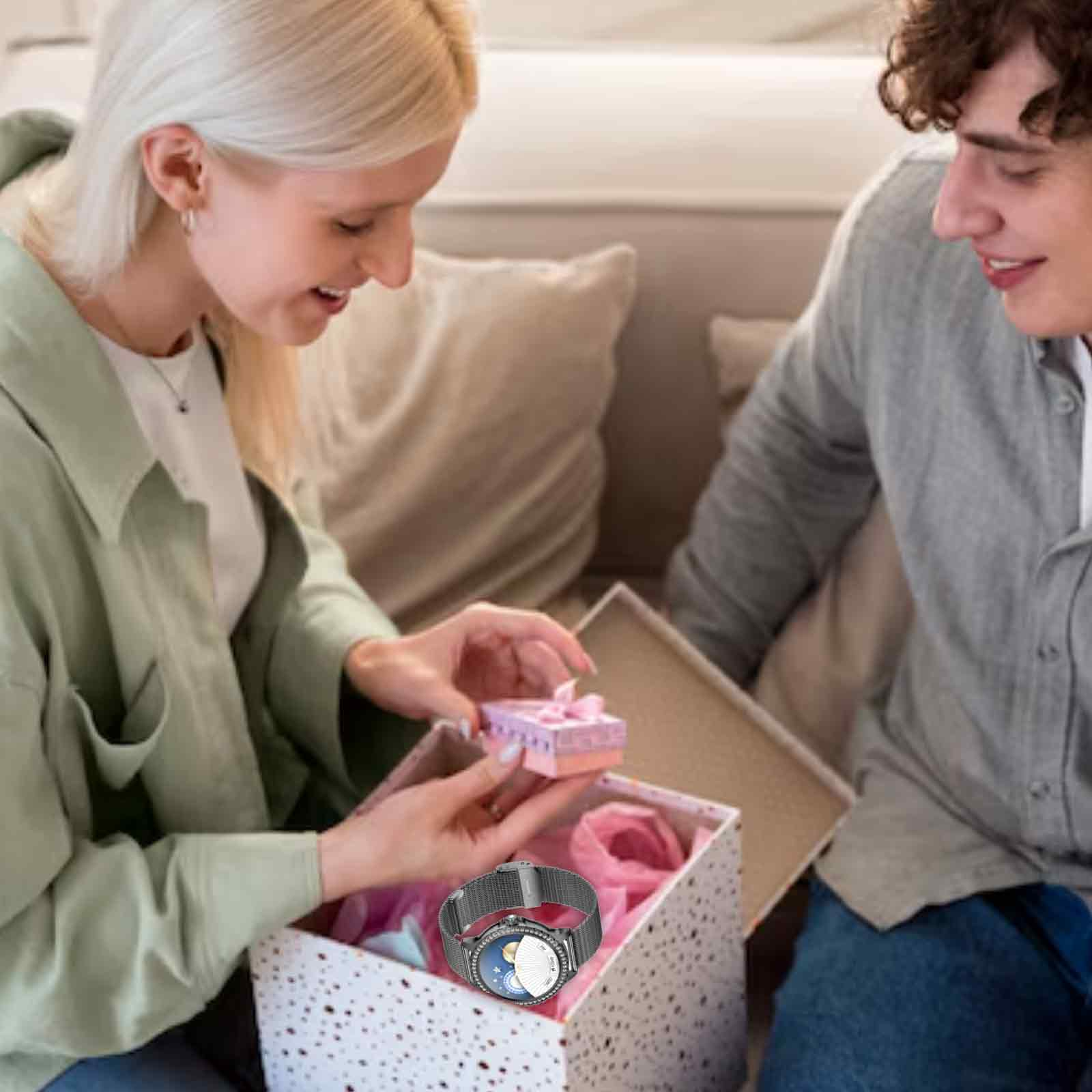 Eine Frau öffnet eine Geschenkbox, um eine Smartwatch zu enthüllen, präsentiert von einem Mann, Sofa im Hintergrund.