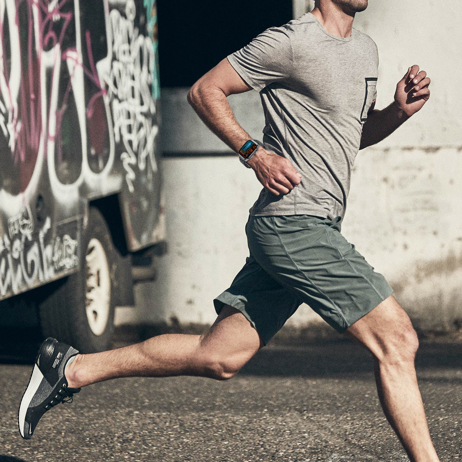 Ein Mann rennt auf einer Straße und trägt ein graues Hemd und Shorts, mit einer Uhr am Handgelenk.
