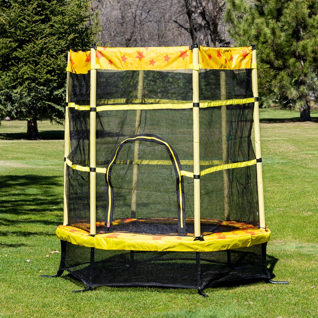 Ein gelb-schwarzes Trampolin mit Netzeinfassung auf grünem Gras mit Bäumen.