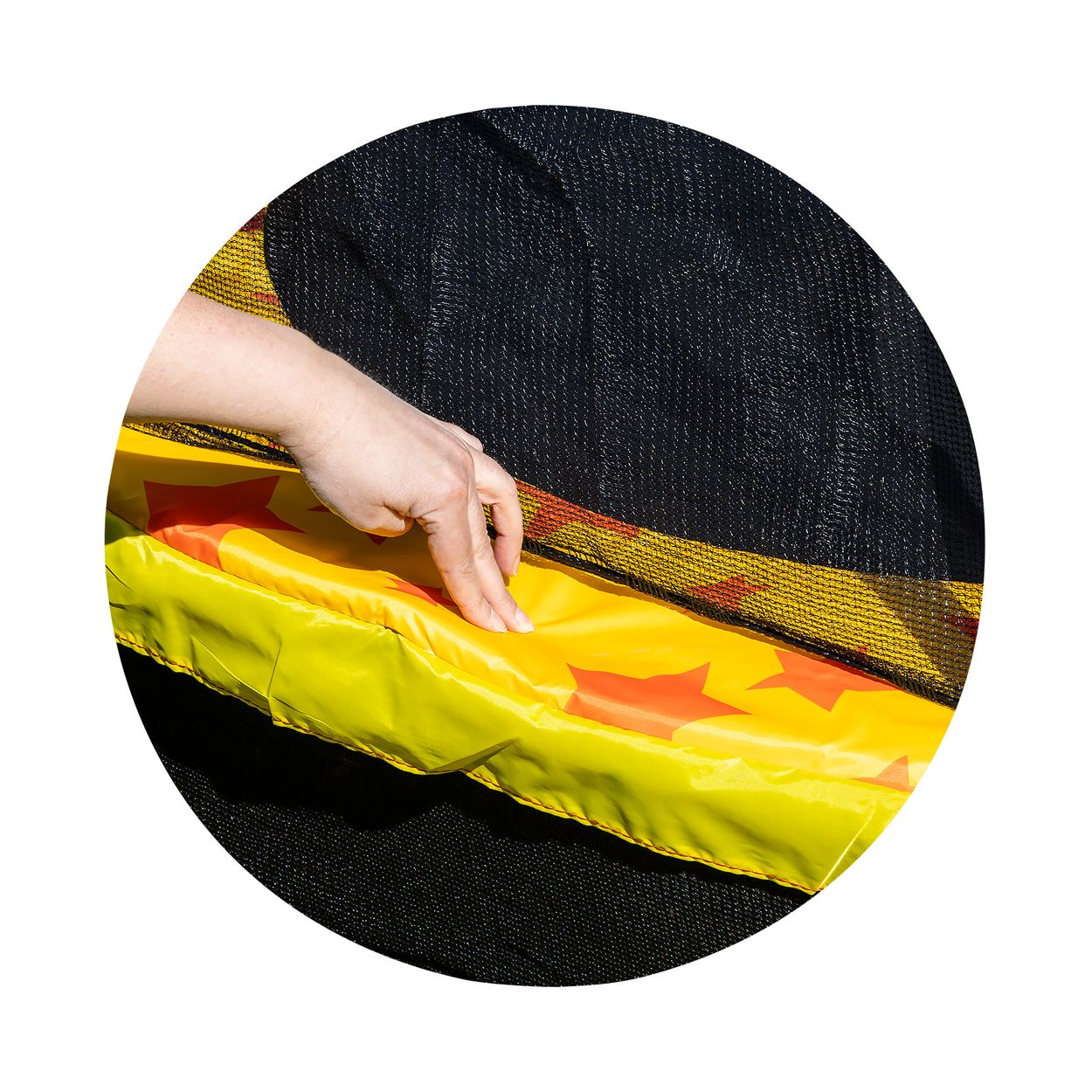 Eine Hand berührt den gelben Rand eines Trampolins mit schwarzem Netz.