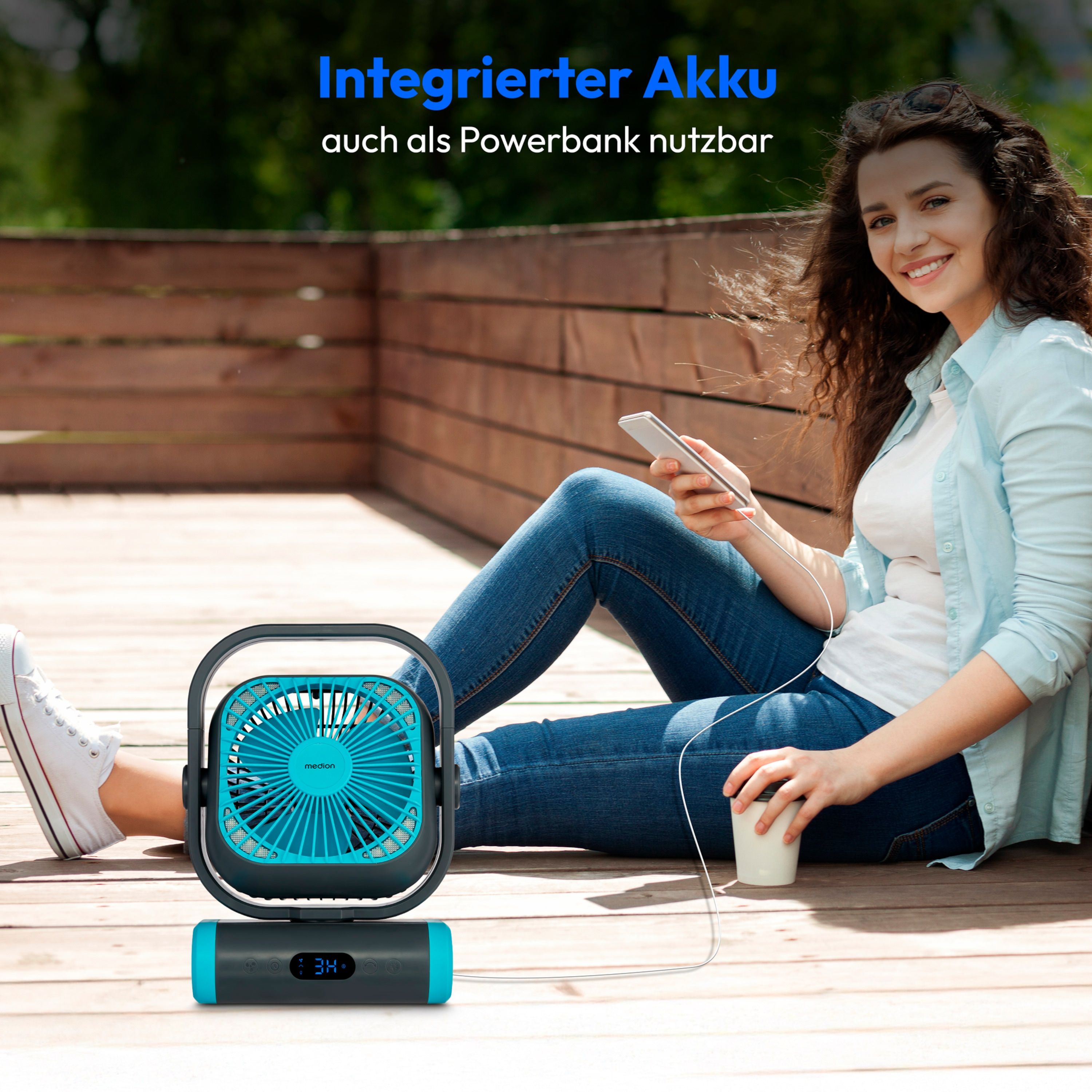 A woman using a phone, with a turquoise and grey fan, sitting on a wooden deck.
