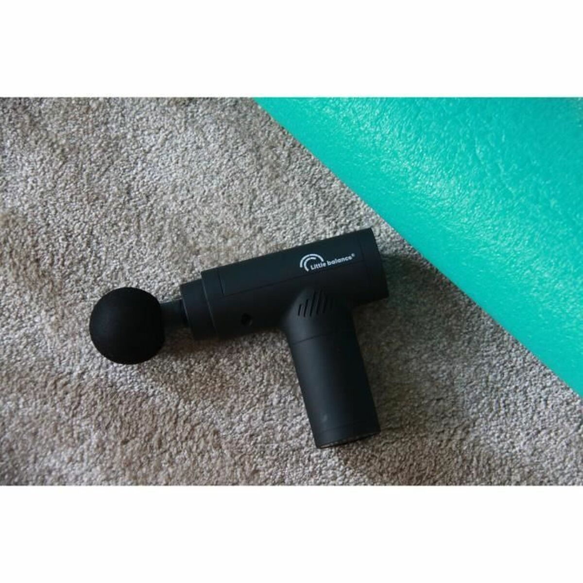 Eine schwarze Massagepistole mit rundem Kopf auf grauem Teppich mit grüner Faszienrolle.