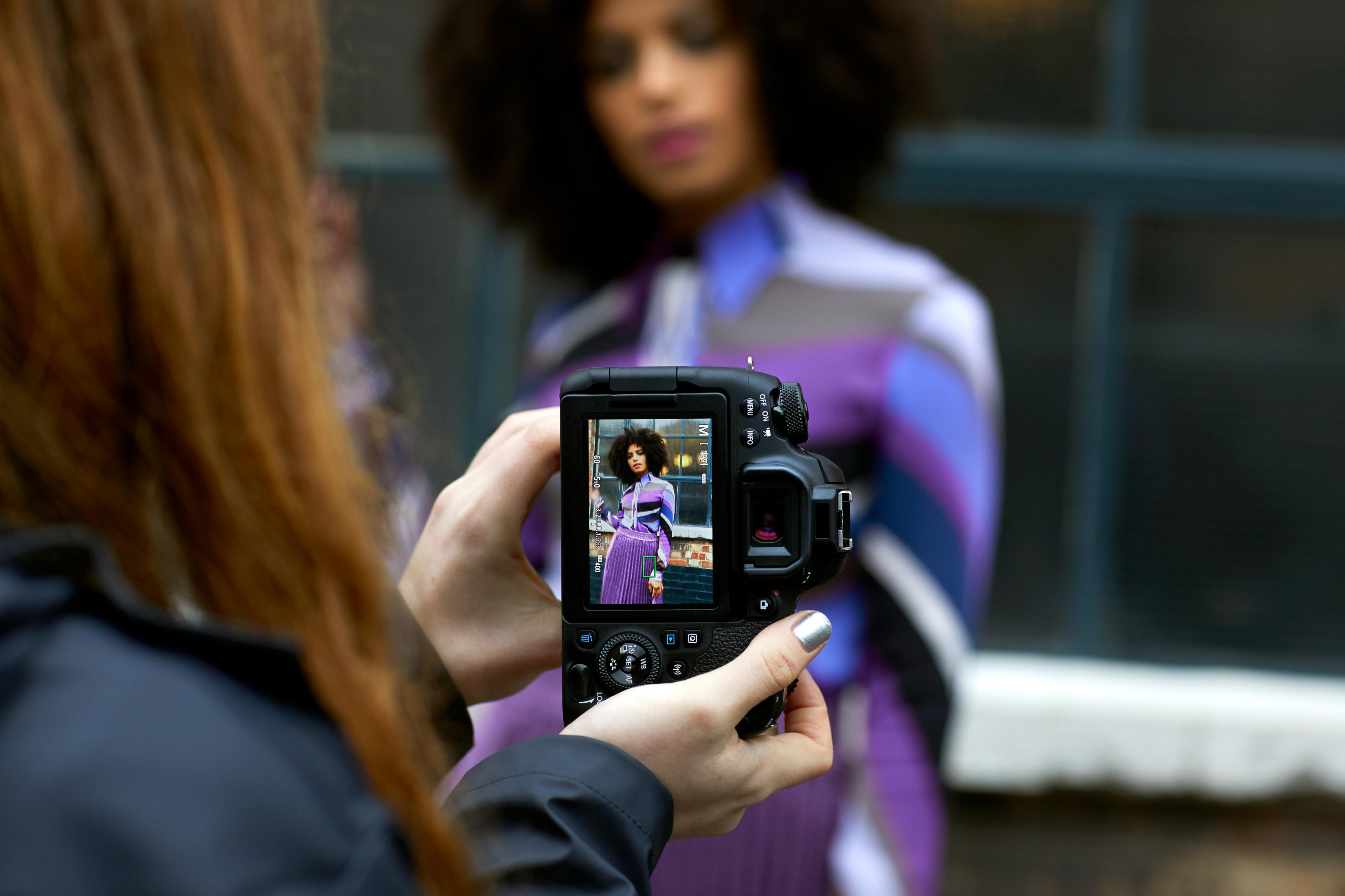 Eine Person hält eine Kamera und fotografiert eine Frau in einem lila Outfit.