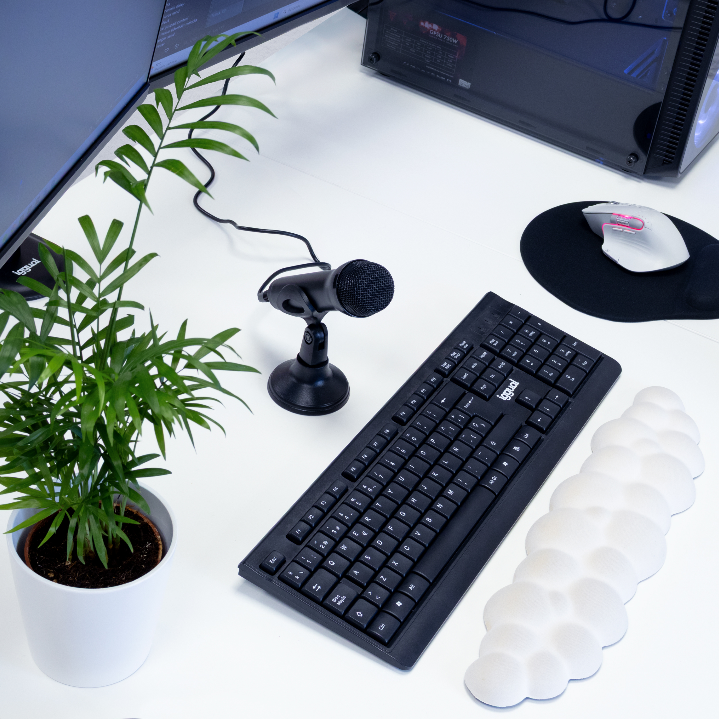 Un escritorio con teclado, planta, micrófono, ratón y alfombrilla de ratón. Una pantalla de ordenador está a la izquierda.