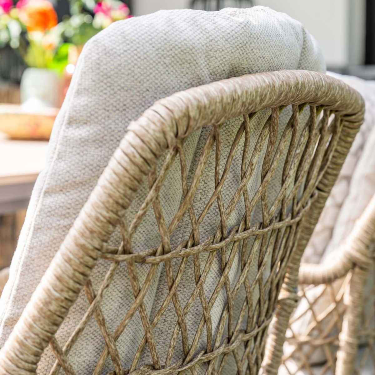 Close-up van een stoel met een geweven rug en een lichtgrijs kussen.