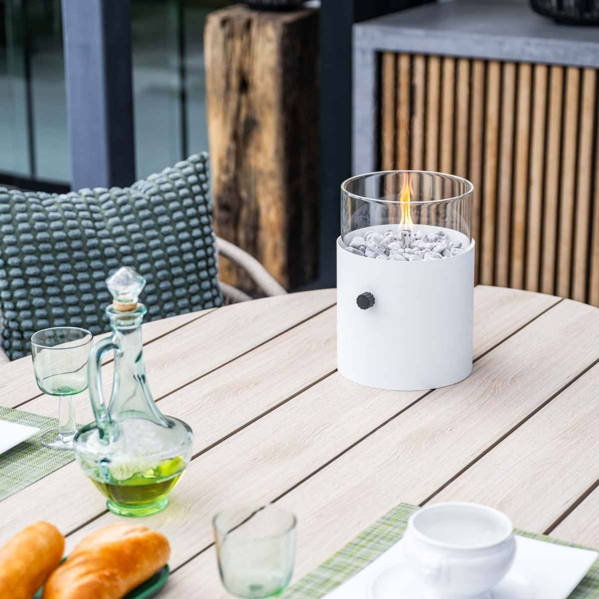 Een tafel met een brandend vuur, een wijnfles, glazen en brood in een buitenomgeving.